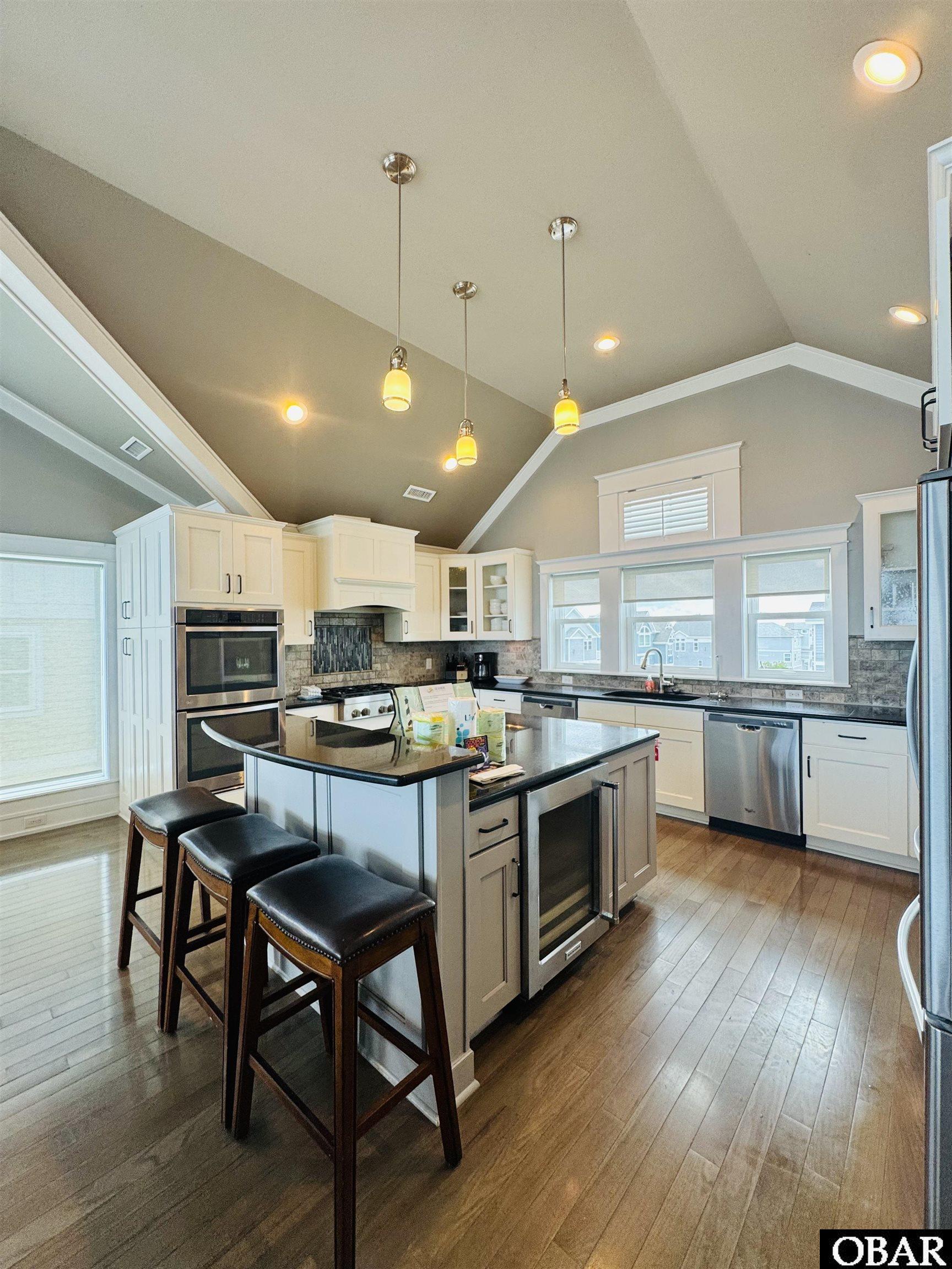Kitchen with vaulted ceilings, white cabinets, stainless appliances, and a large island with three stools.