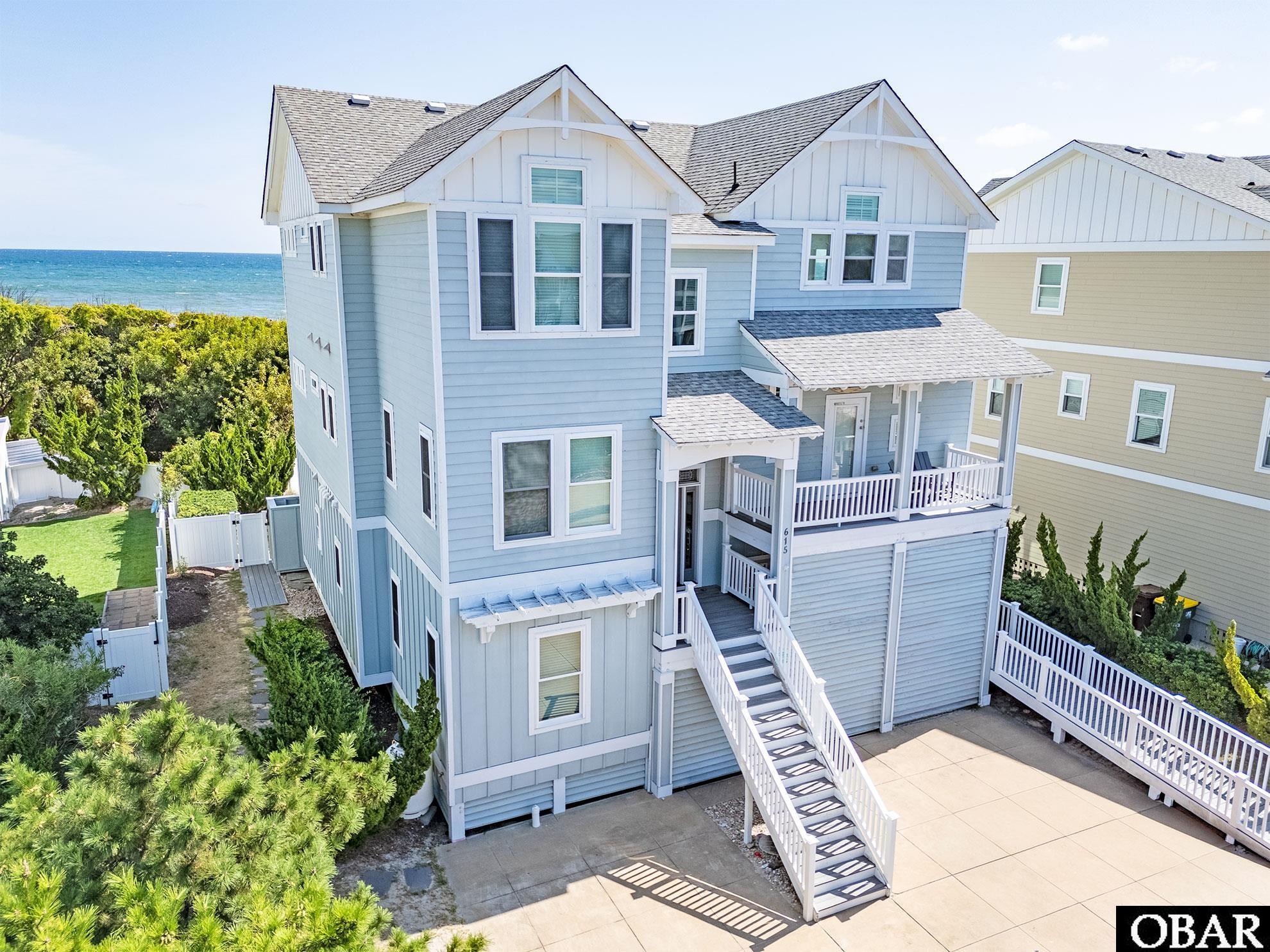Light blue coastal home with white porches and stairs, photographed from above with the ocean behind it.