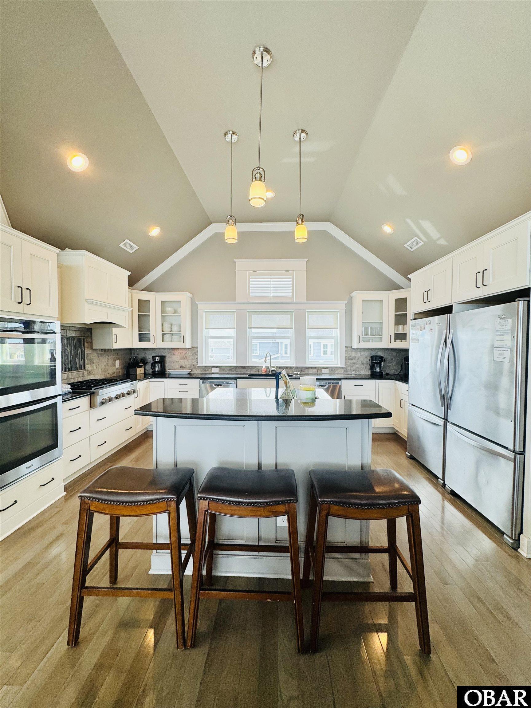 Kitchen with a large island, three bar stools, white cabinets, and stainless steel appliances.