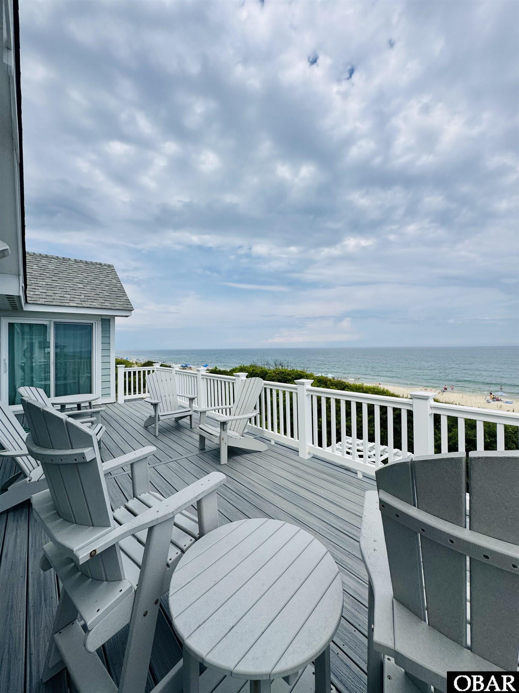 Oceanfront deck with Adirondack chairs and a round table overlooking the beach and water.