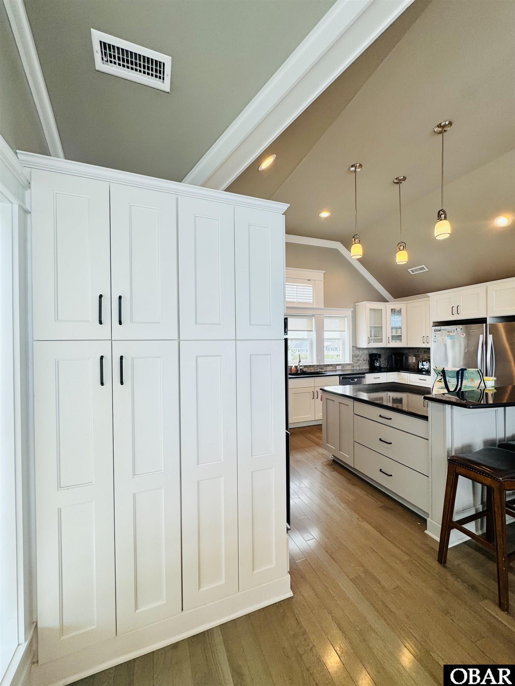 Kitchen with white paneled cabinets, a large black-countertop island, pendant lights, and wood flooring.