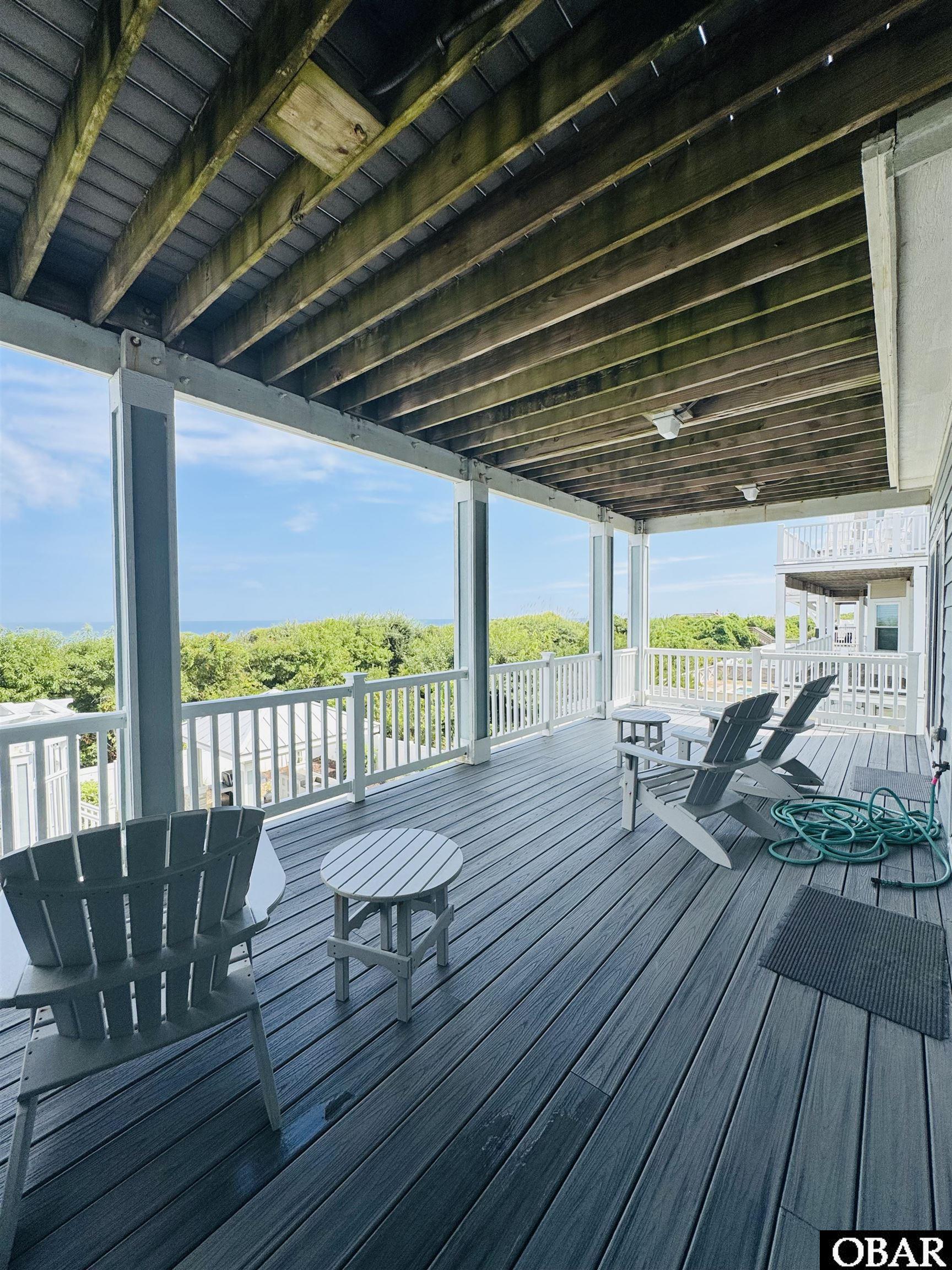 Covered deck with Adirondack chairs and a glimpse of ocean beyond the railing.