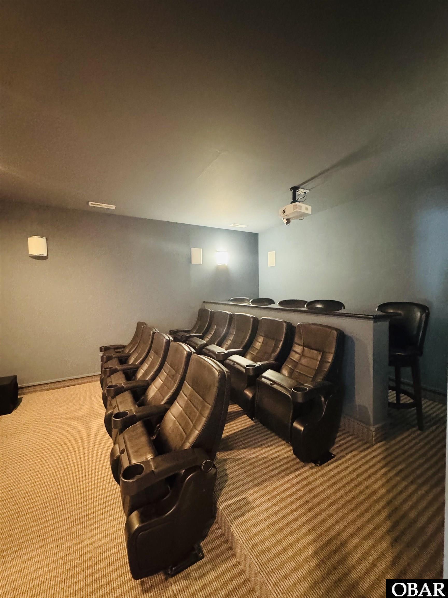 Home theater with rows of brown leather recliners, a ceiling projector, and a raised counter with bar stools.