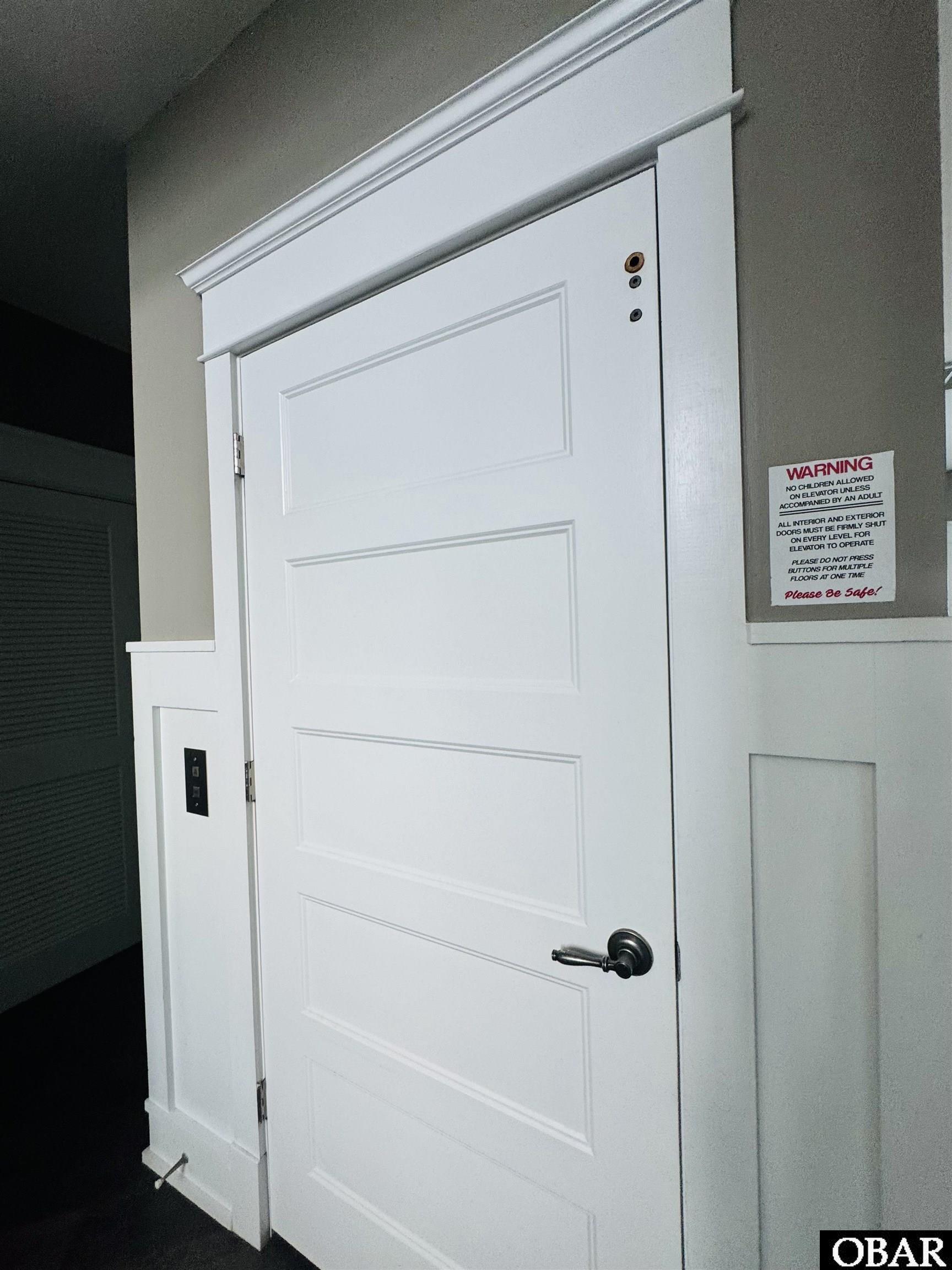 Closed white paneled elevator door with a metal handle and safety notice beside it.