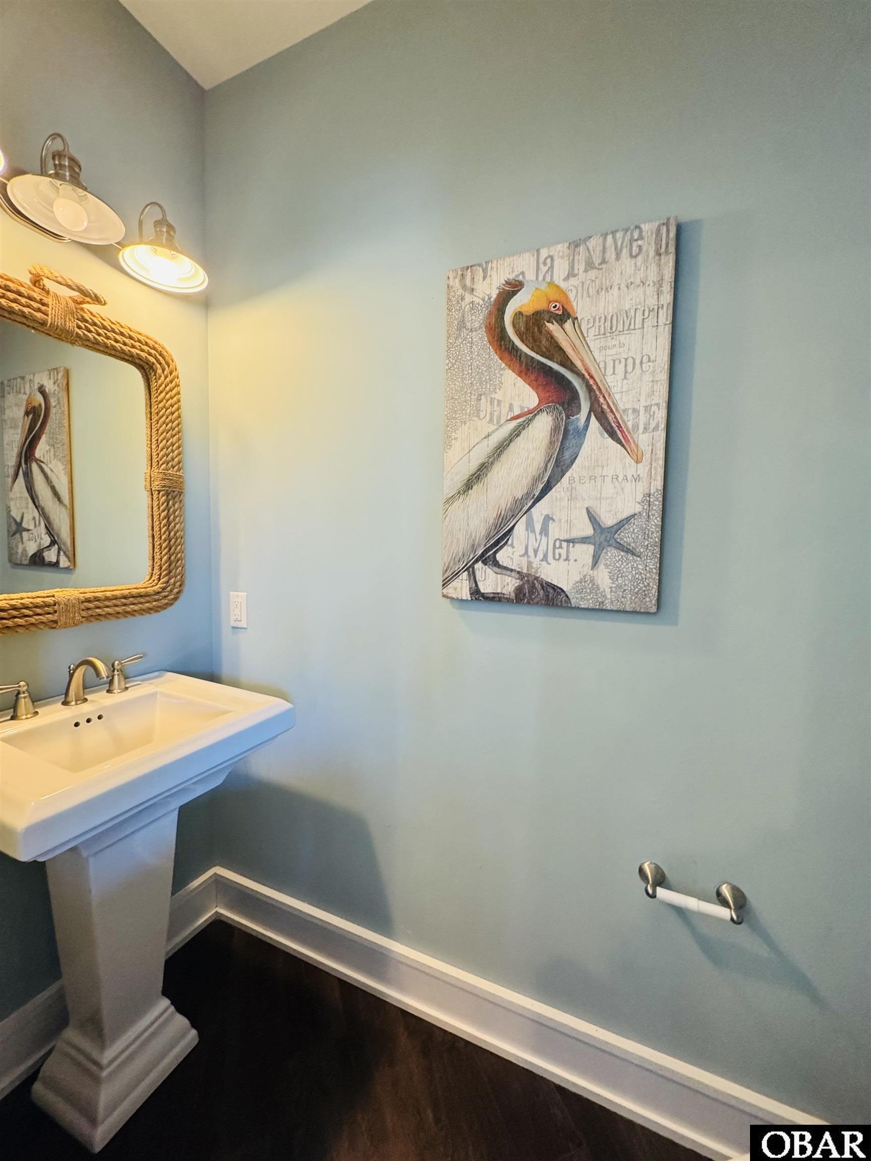 Bathroom with a white pedestal sink, rope-framed mirror, and pelican wall art.