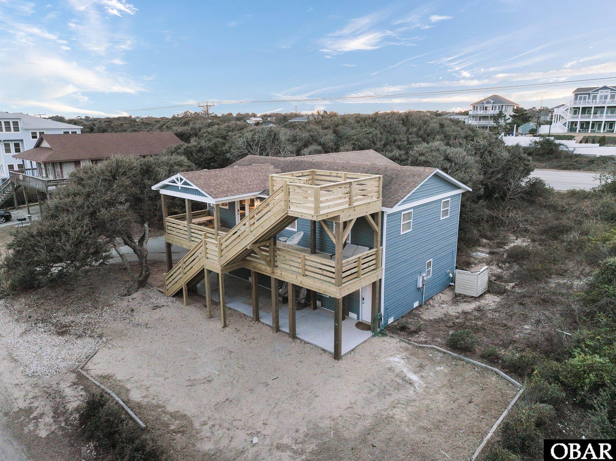 Blue coastal home with large raised wooden decks and stairs, viewed from above.