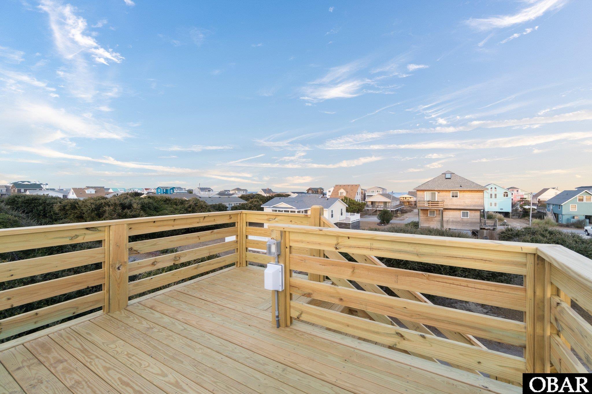 Raised wooden deck overlooking a neighborhood of coastal-style homes beneath a broad blue sky.