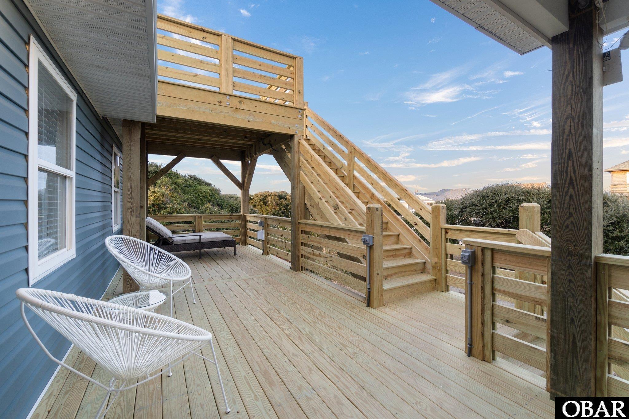 Wooden house deck with white woven chairs and stairs to an upper deck.