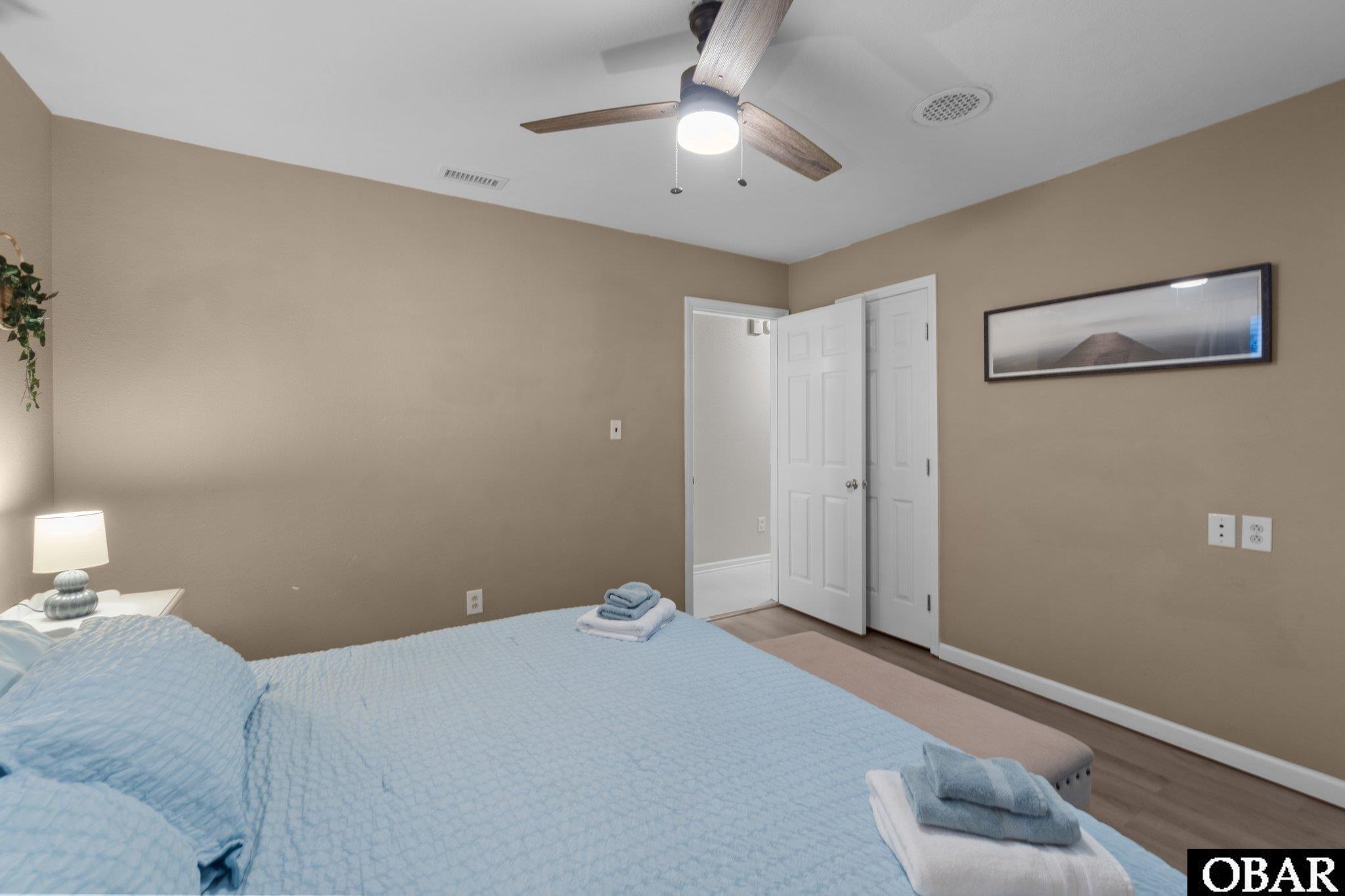 Bedroom with a light blue bedspread, folded towels, and a ceiling fan.