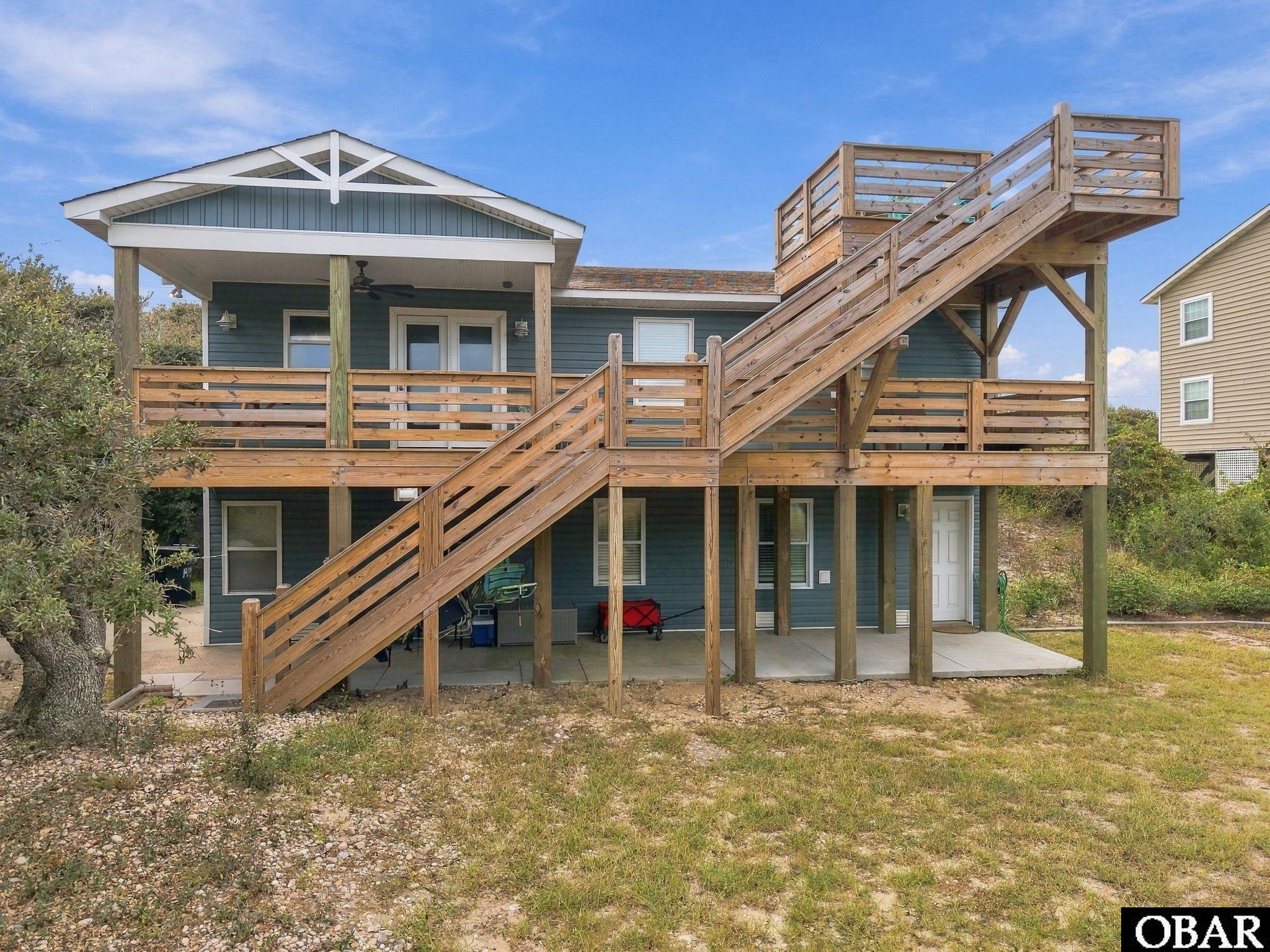 Blue coastal home with expansive wooden decks and long exterior stairs to a rooftop deck.
