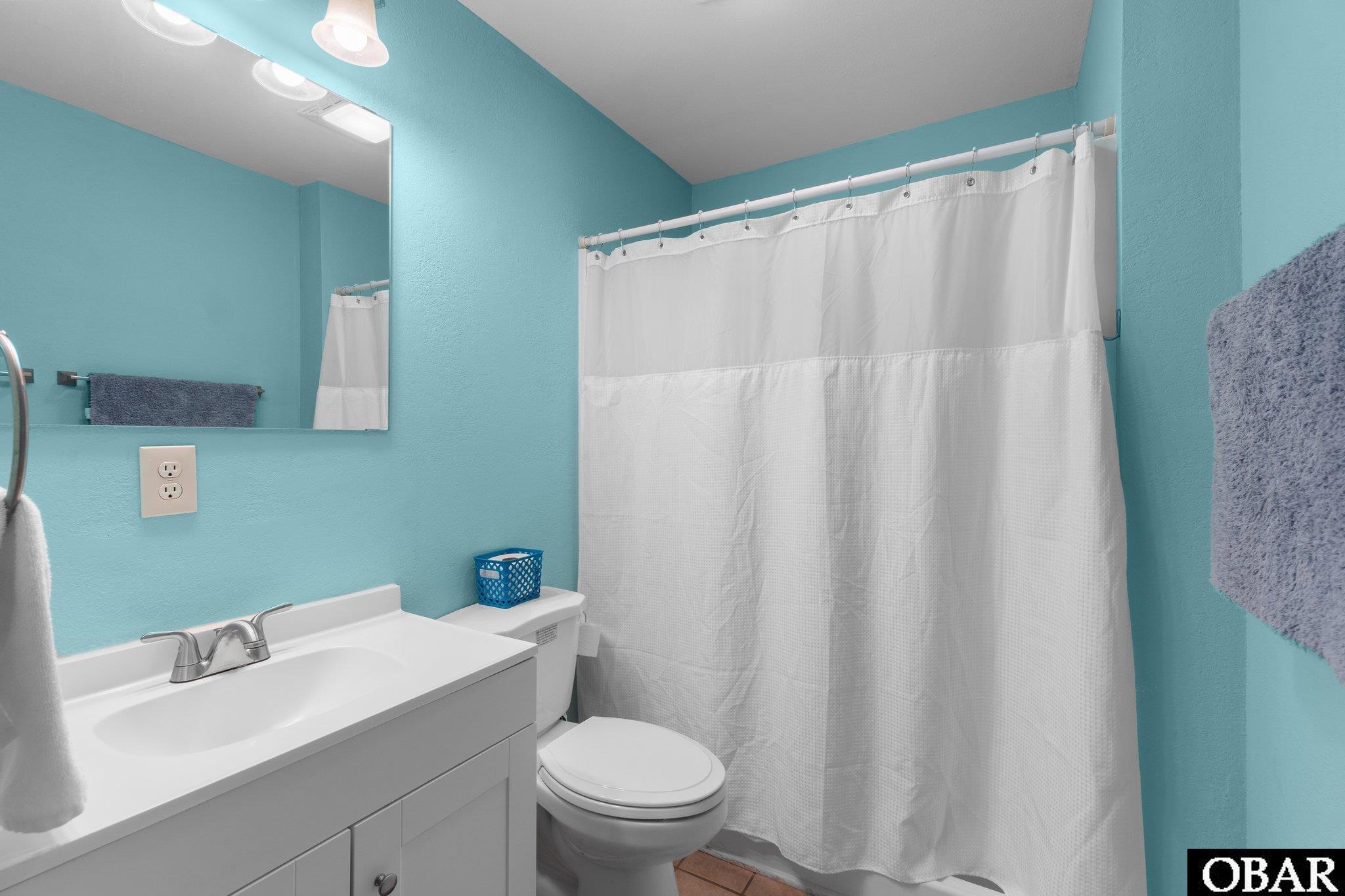 Bathroom with turquoise walls, white vanity, toilet, and a white shower curtain.