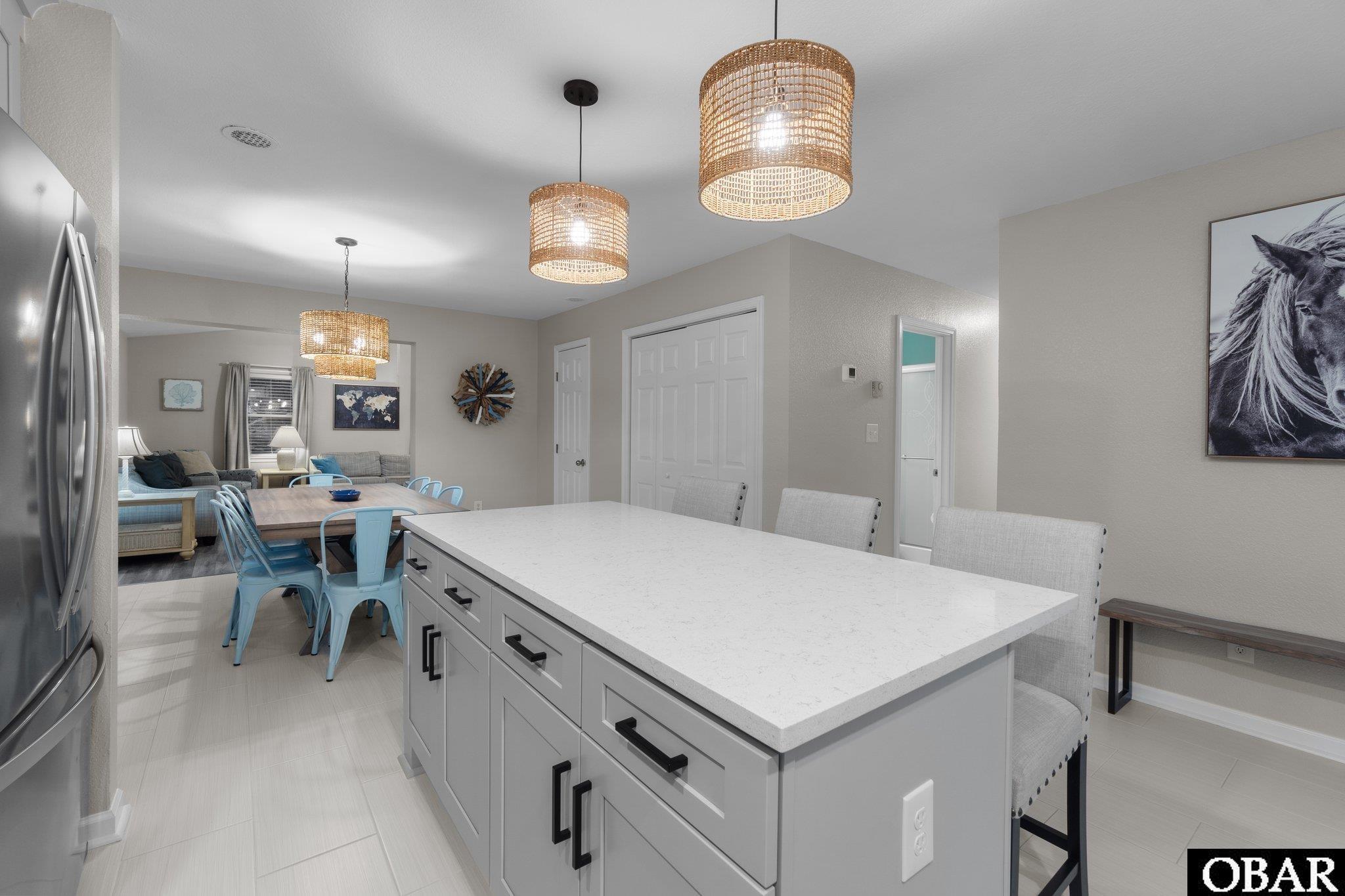 Kitchen and dining area with a large white island, woven pendant lights, and blue chairs.