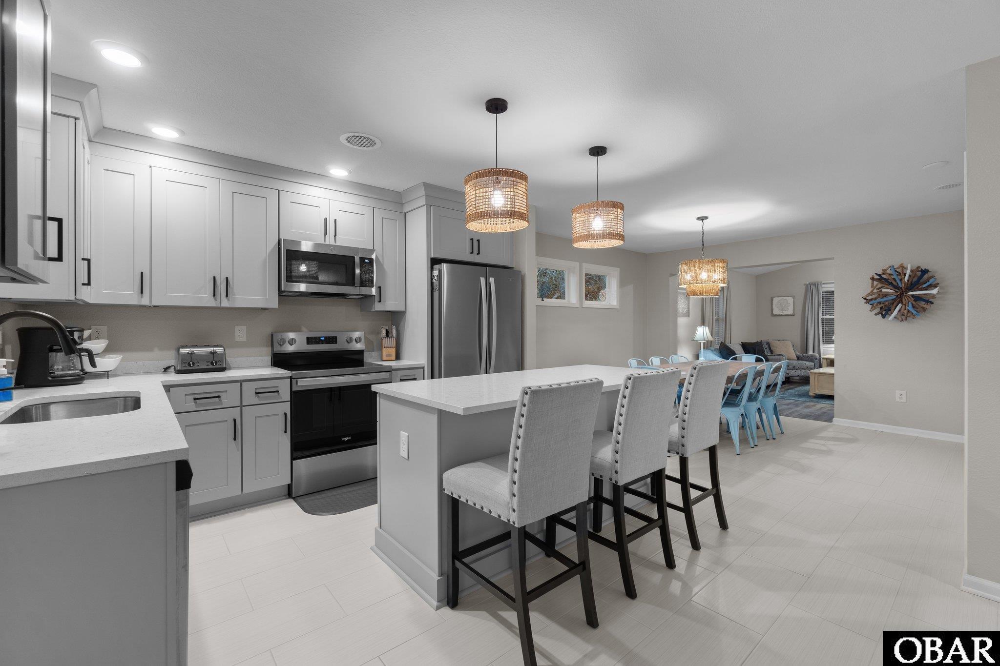 Open-plan kitchen with a large island, white cabinets, stainless steel appliances, and adjoining dining and living areas.