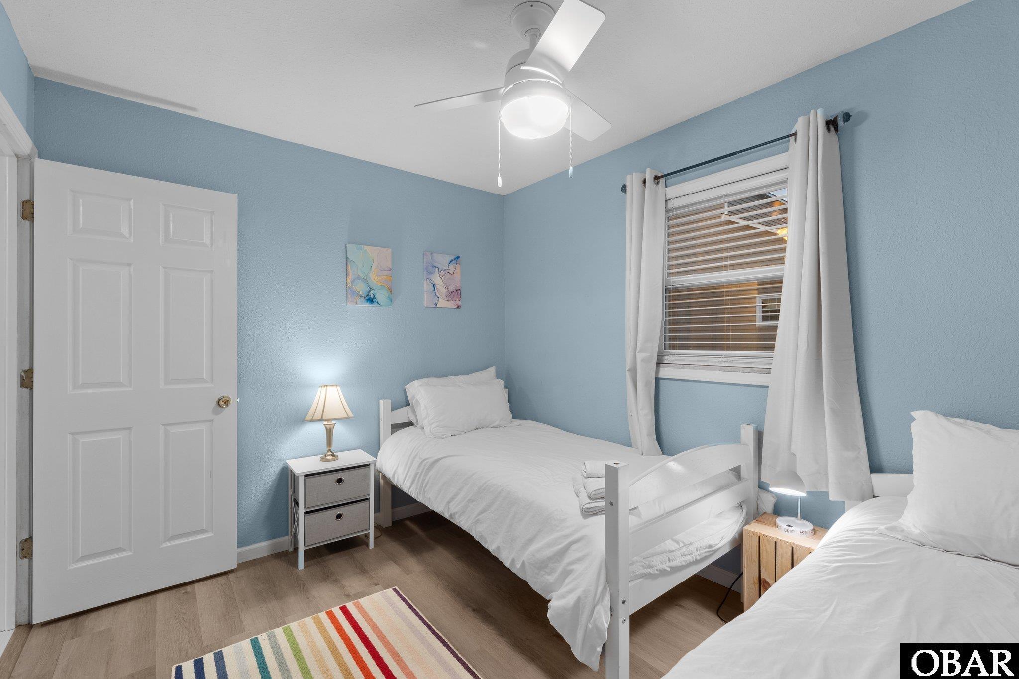 Bedroom with two white twin beds, pale blue walls, and a colorful striped rug.