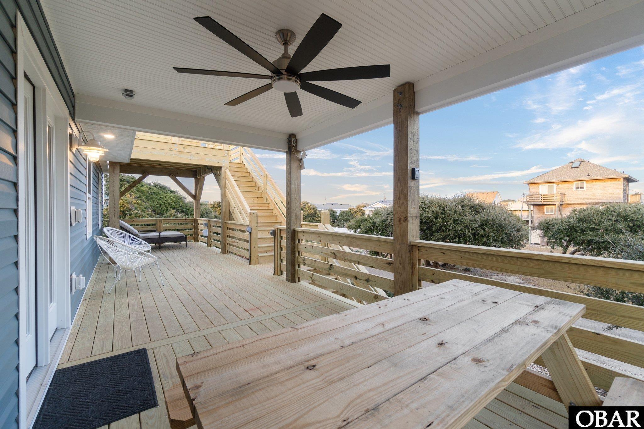 Covered wooden deck with a ceiling fan, stairs, white chairs, and a picnic table.