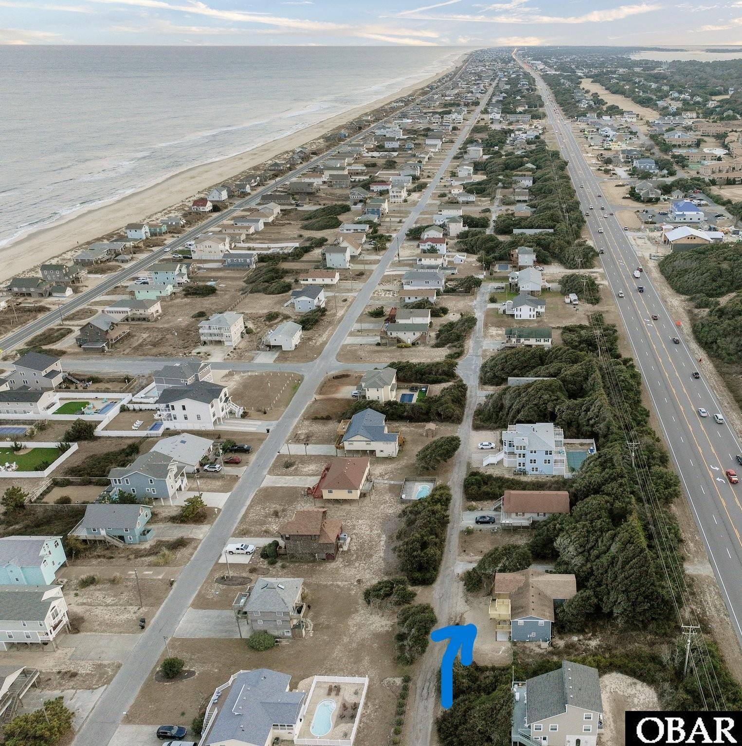Aerial view of a Kitty Hawk coastal neighborhood, with beach, highway, and blue arrow marking a property.