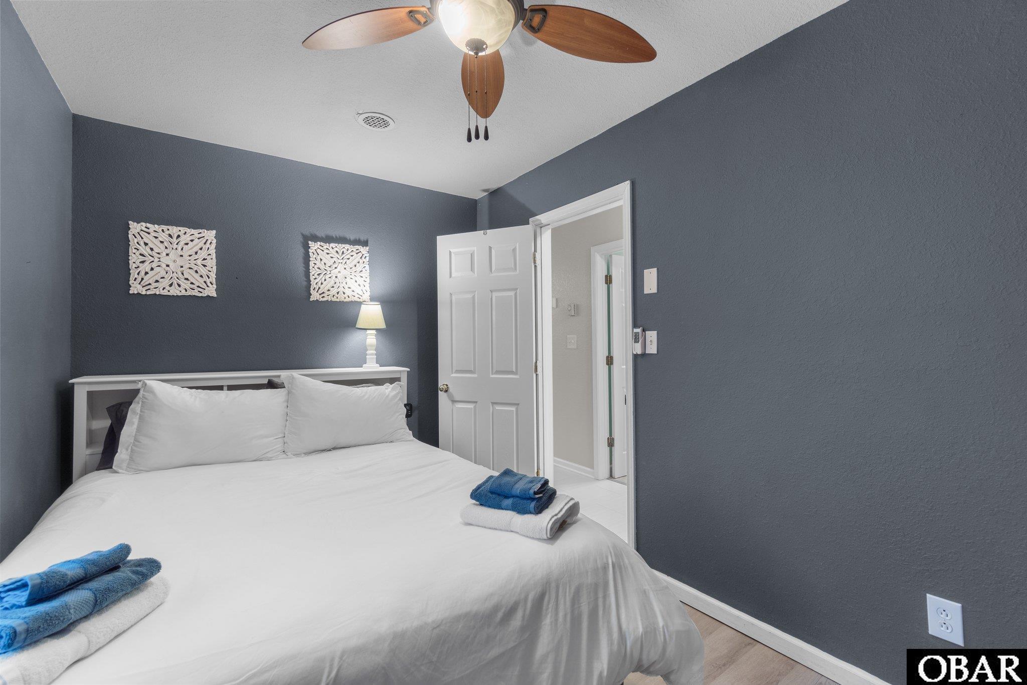 Bedroom with a white bed, blue-gray walls, folded towels, and an open doorway.