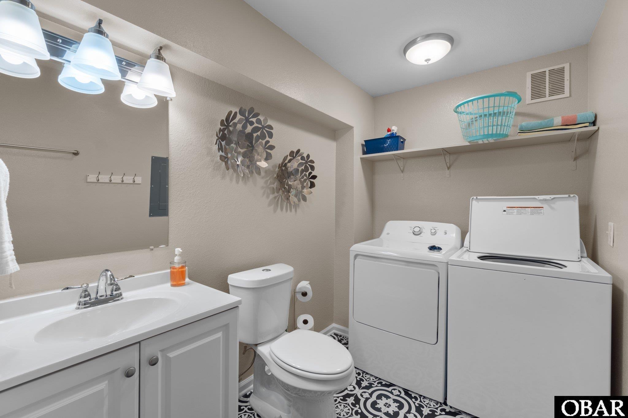 Bathroom and laundry area with a white vanity, toilet, washer, dryer, and patterned tile floor.