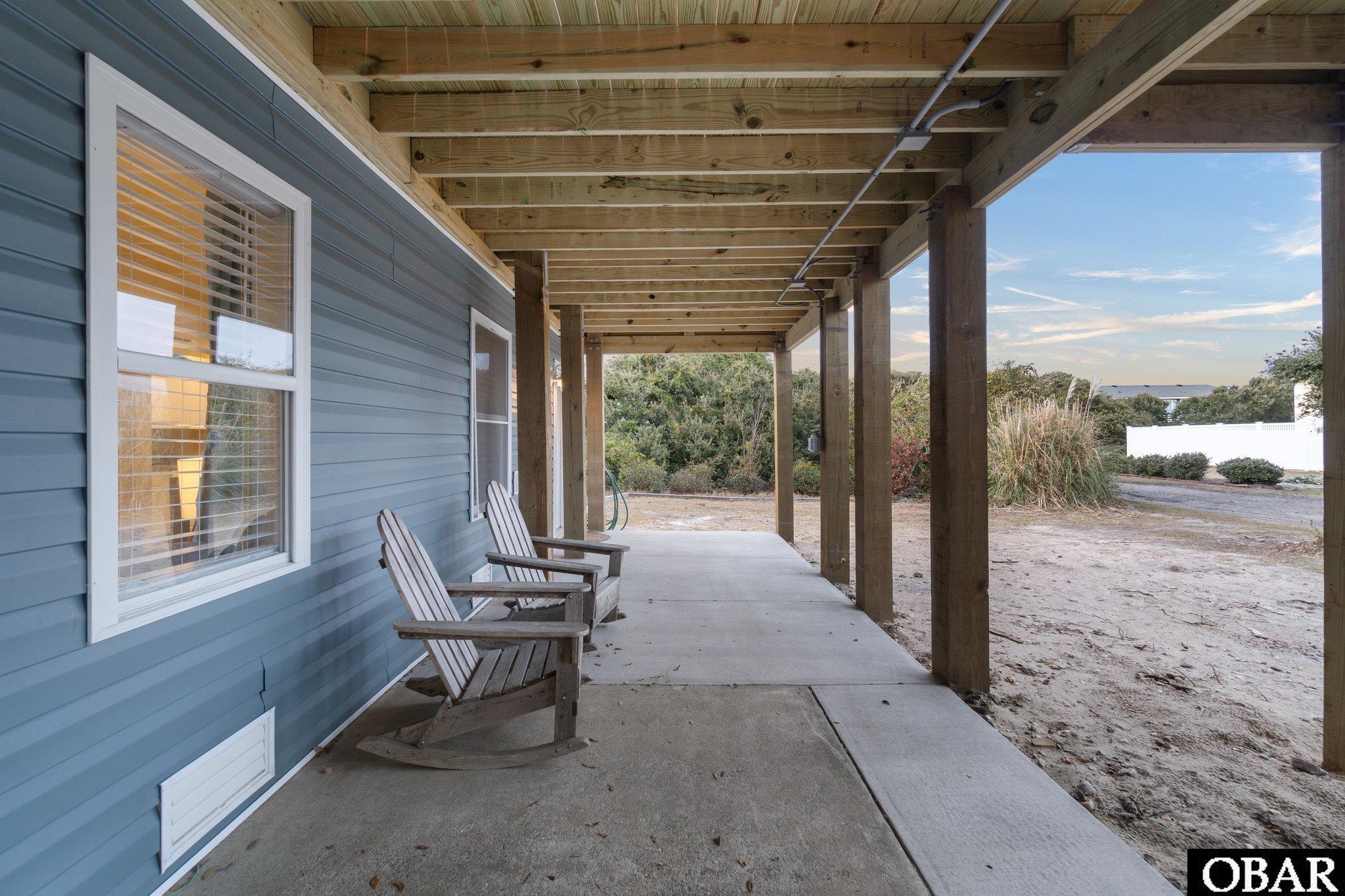 Covered porch with exposed wood beams and two rocking chairs beside blue siding.
