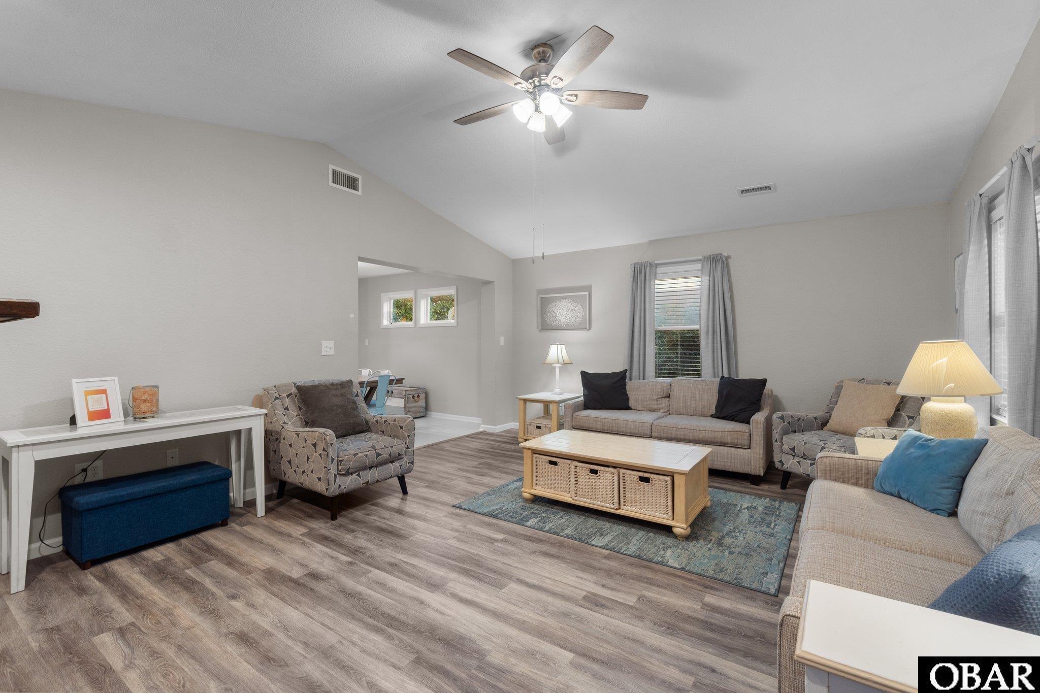 Furnished living room with vaulted ceiling, gray seating, patterned armchairs, and a blue area rug.