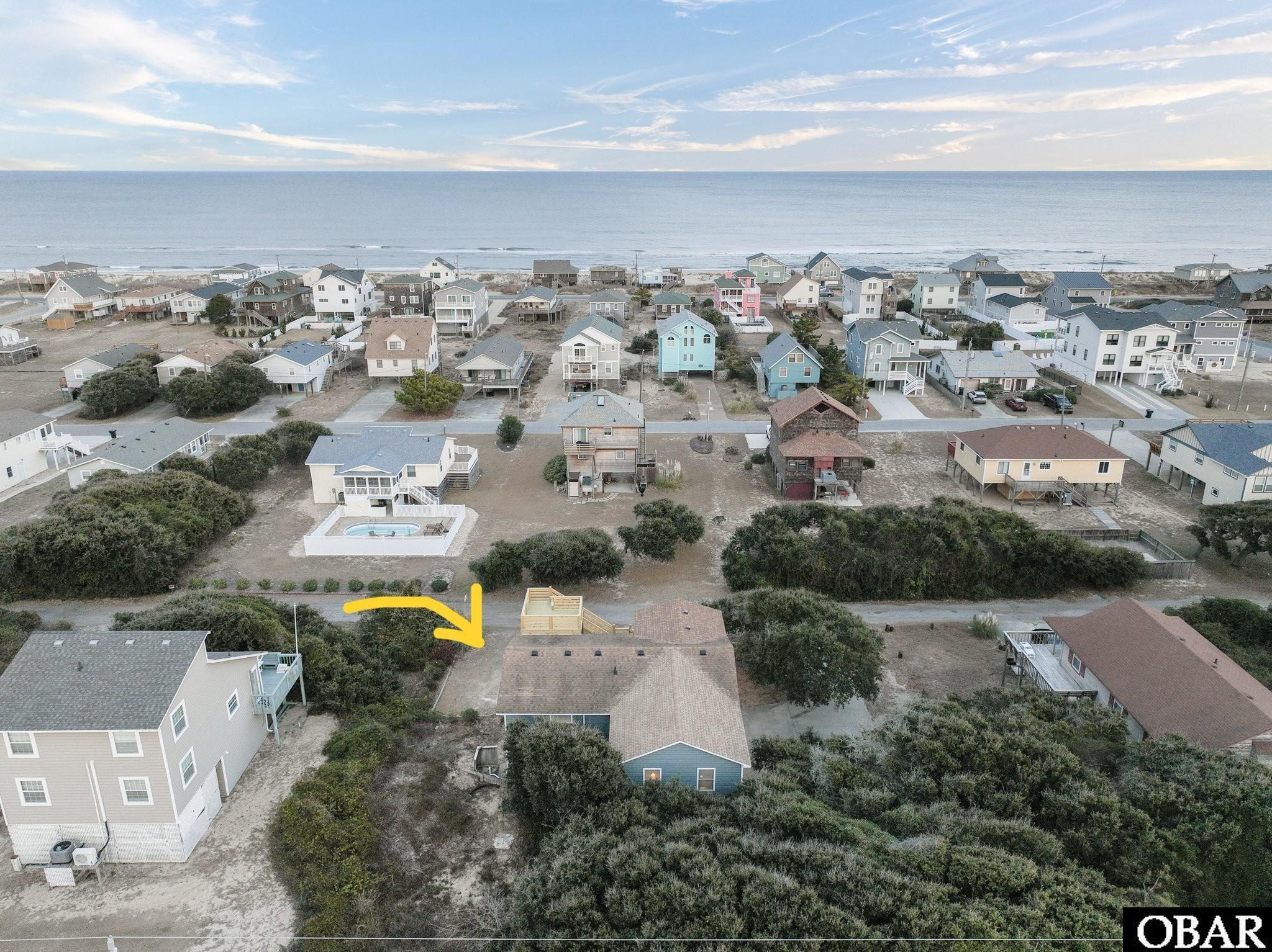 Aerial view of a blue-roofed coastal home marked by a yellow arrow, with ocean beyond.