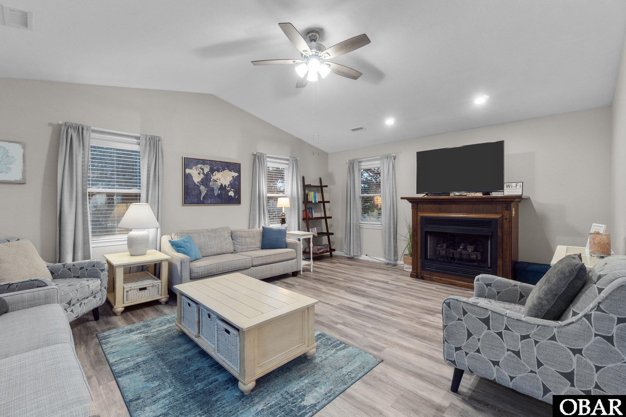 Furnished living room with a television above a dark wood fireplace and seating around a blue rug.