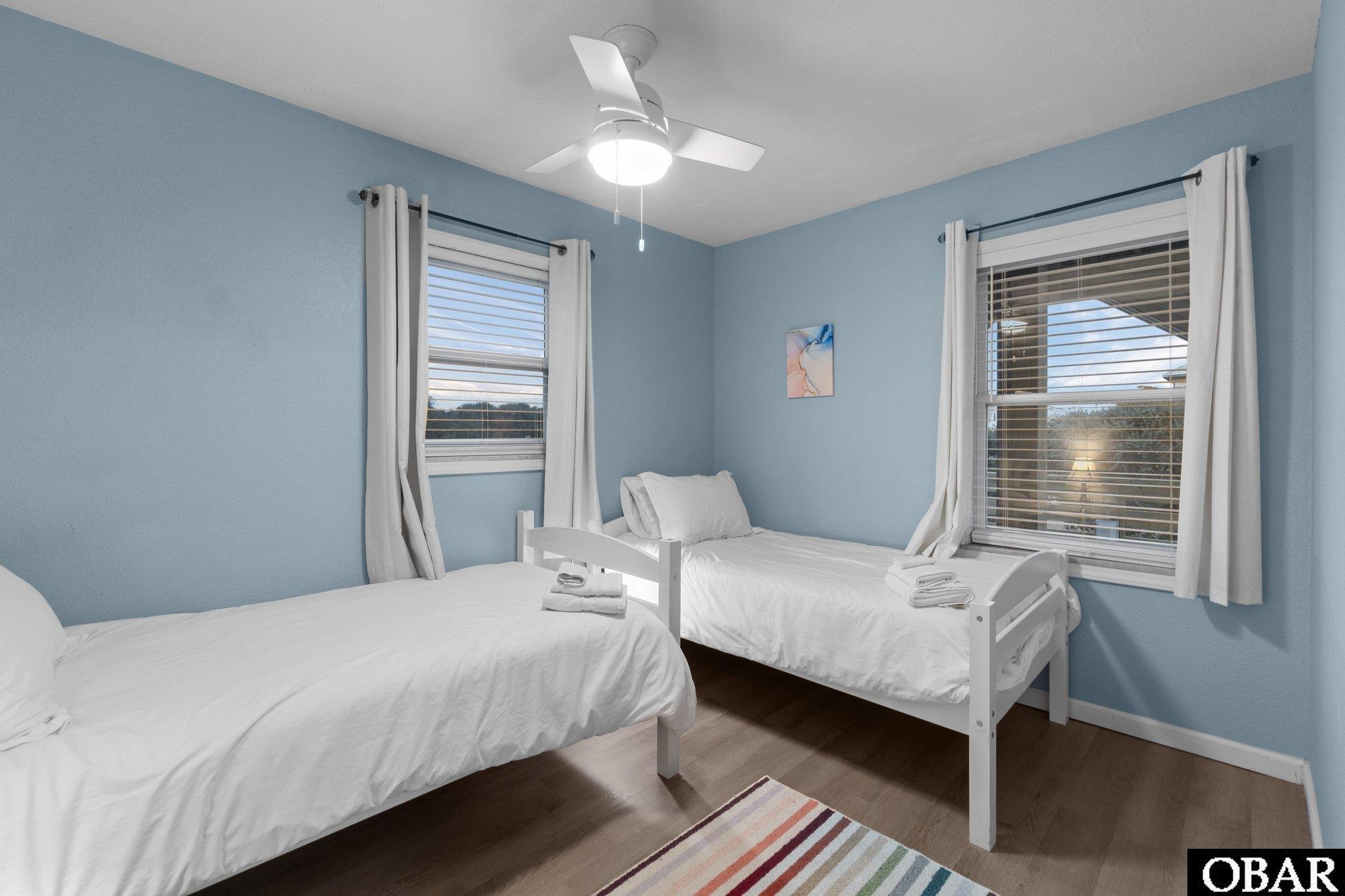 Bedroom with two white twin beds, blue walls, and windows with blinds and white curtains.
