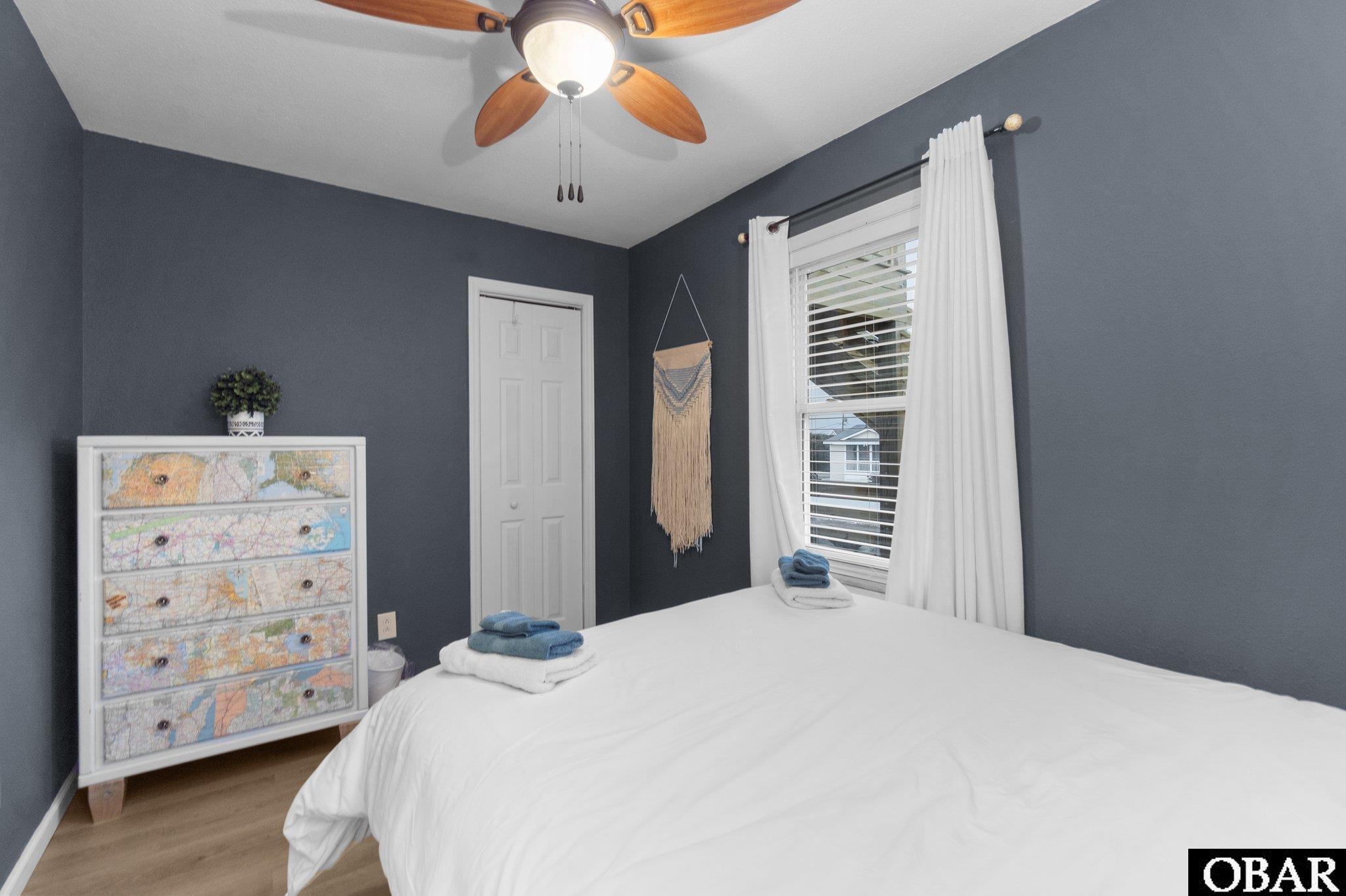 Bedroom with a white bed, map-front dresser, and window framed by white curtains.