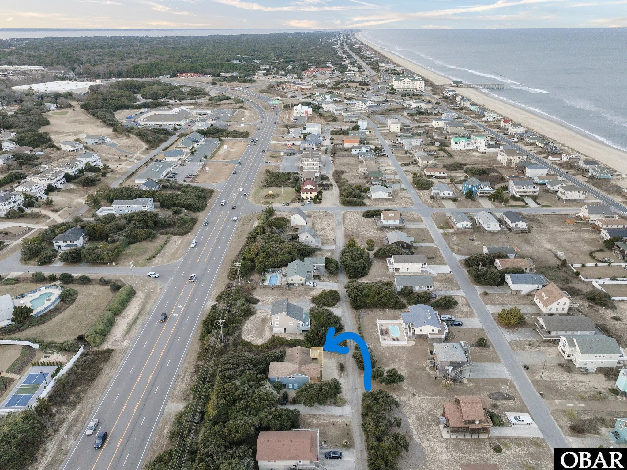 Aerial view of the coastal neighborhood, with a blue arrow marking the property near the beach and highway.