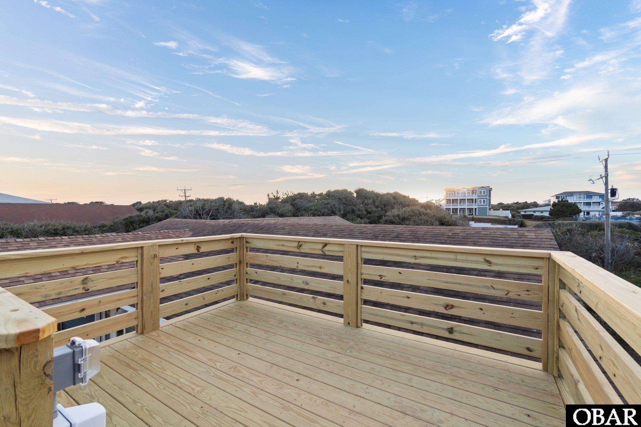 Elevated wooden deck overlooking rooftops and trees beneath a cloud-streaked sky.