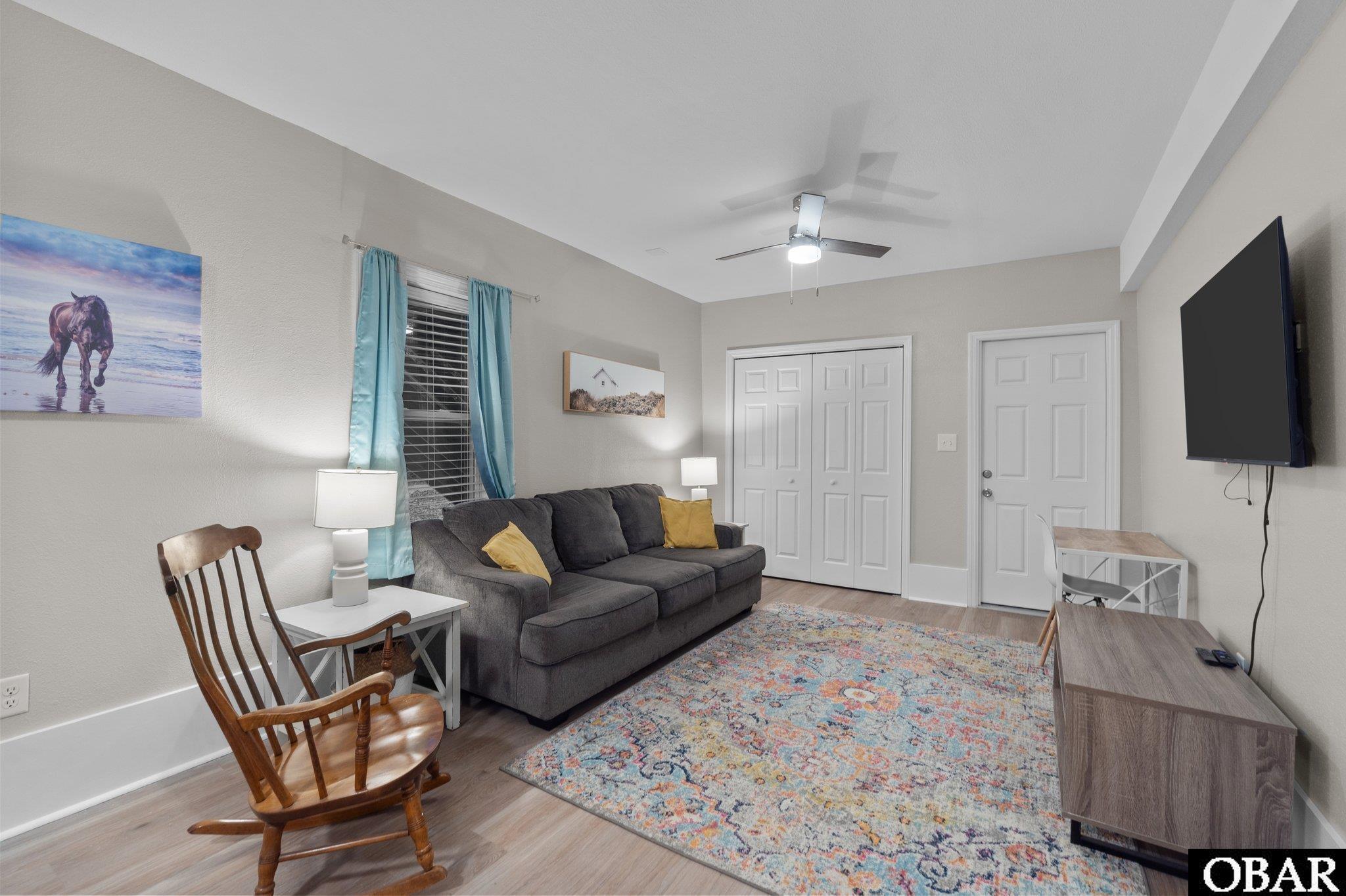 Living room with a gray sofa, wooden rocking chair, colorful rug, and wall-mounted television.