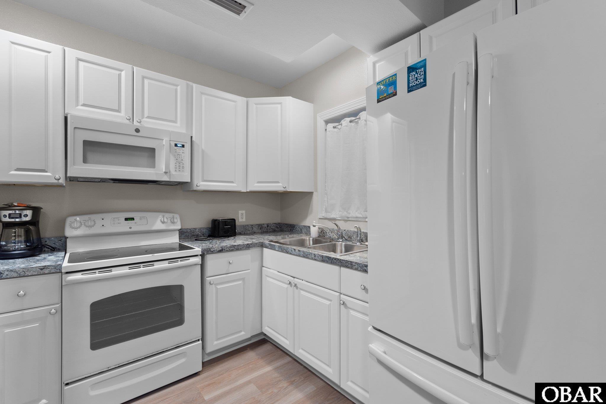Kitchen with white cabinets, speckled counters, a double sink, and white appliances.