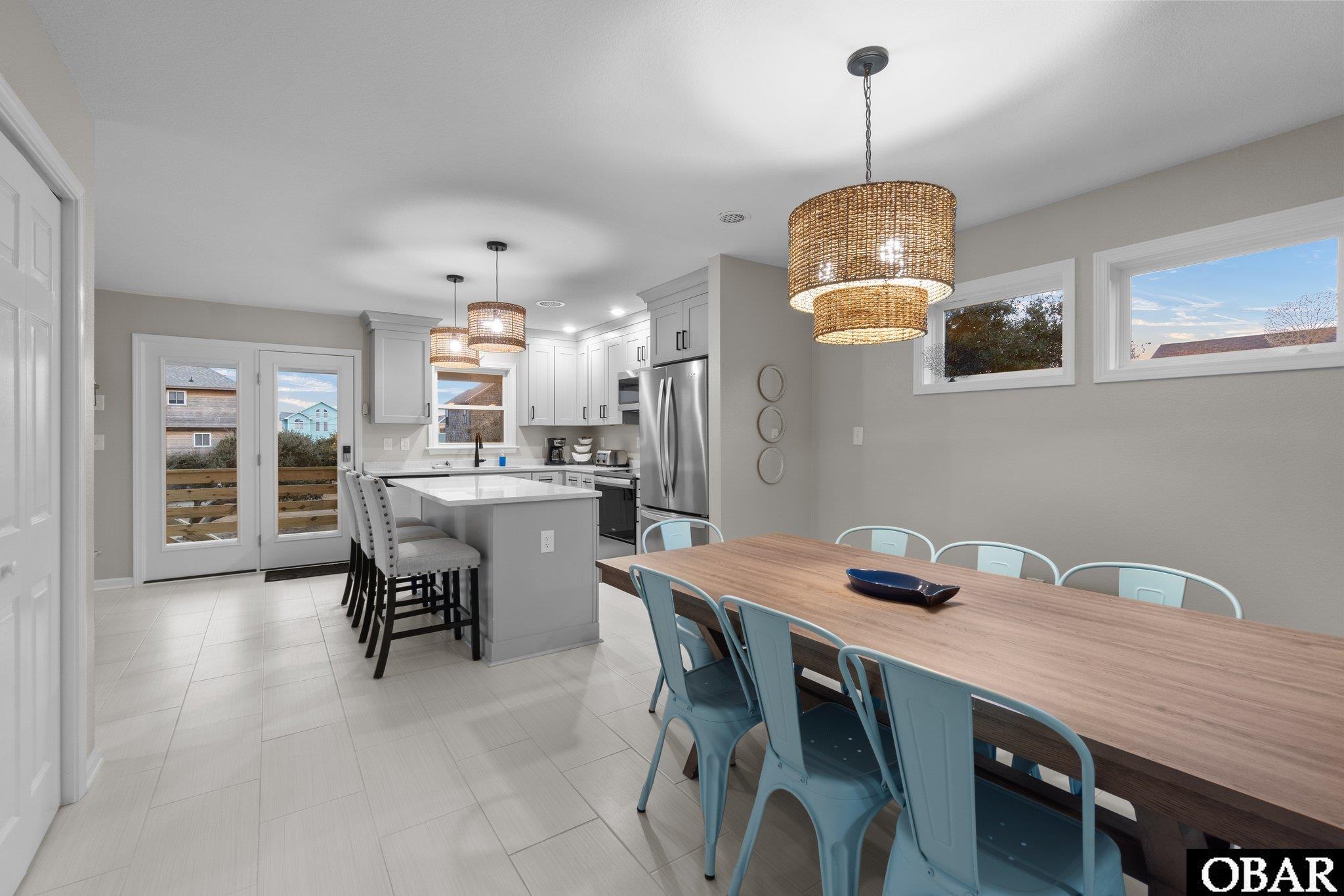 Open-plan kitchen and dining area with a large island, woven pendant lights, and a long wood table.