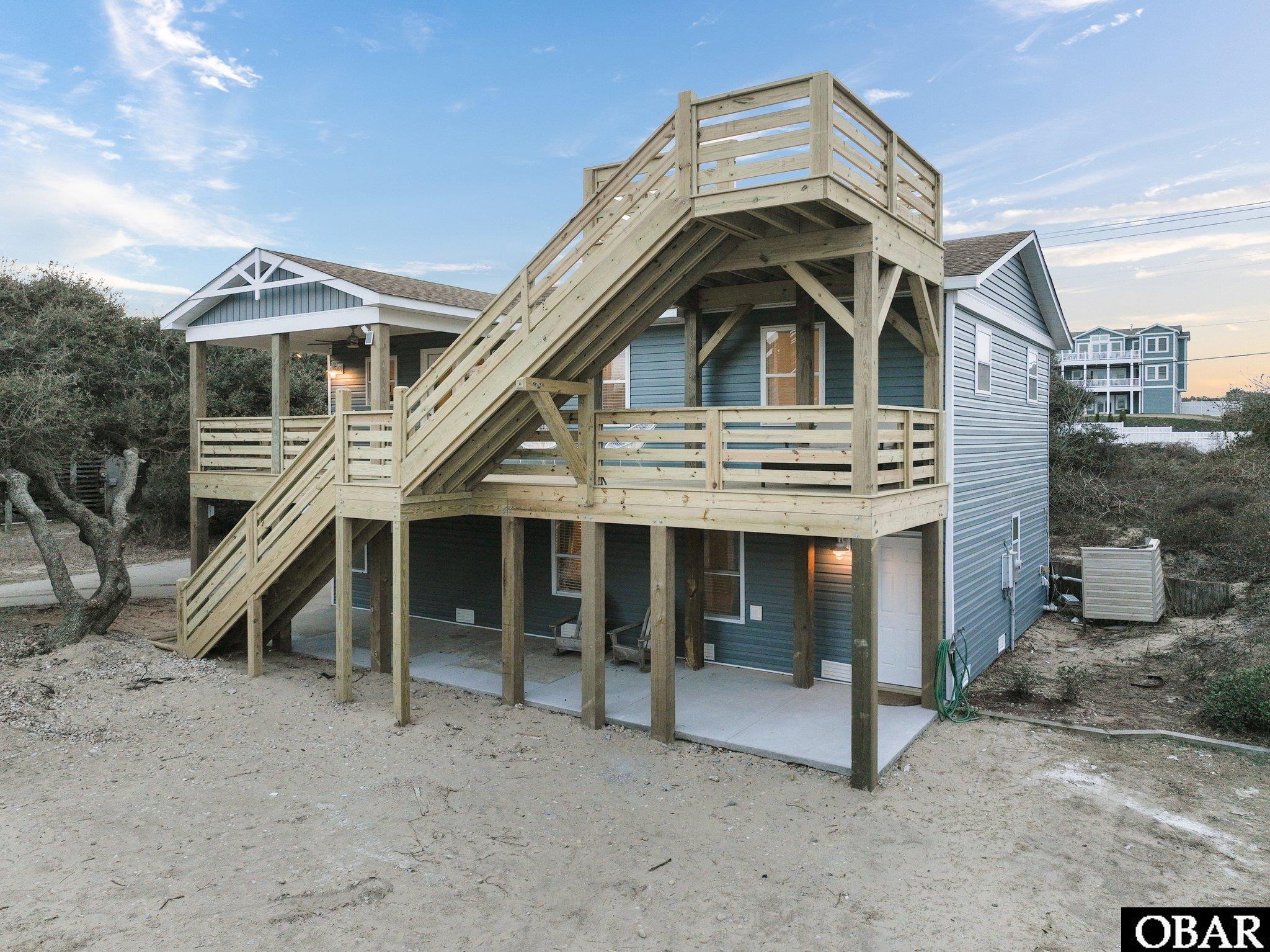 Blue-sided home with a large elevated wooden deck, prominent outdoor staircase, and covered patio.
