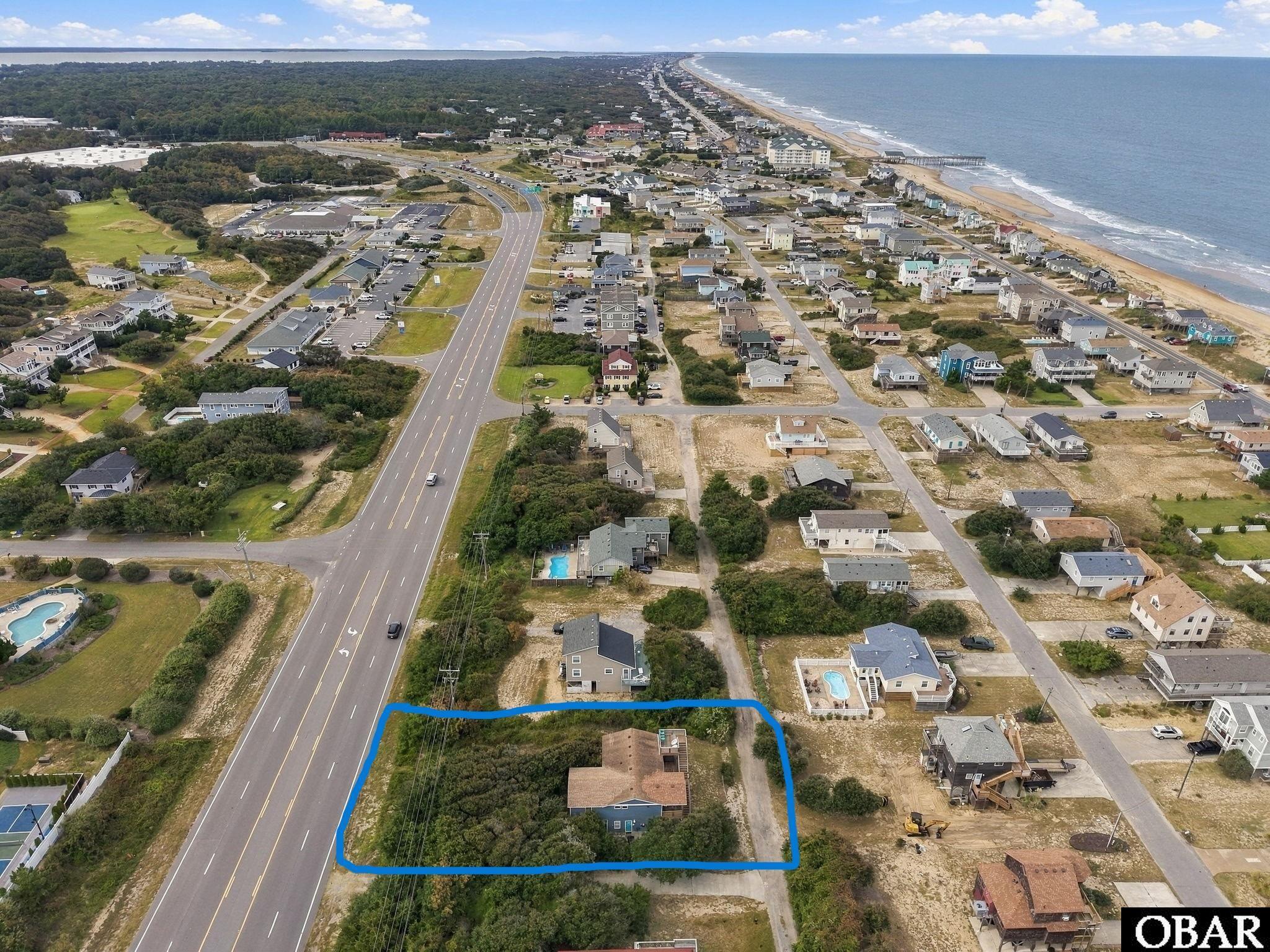 Aerial view of a blue-outlined home beside a major road, with the ocean in the distance.