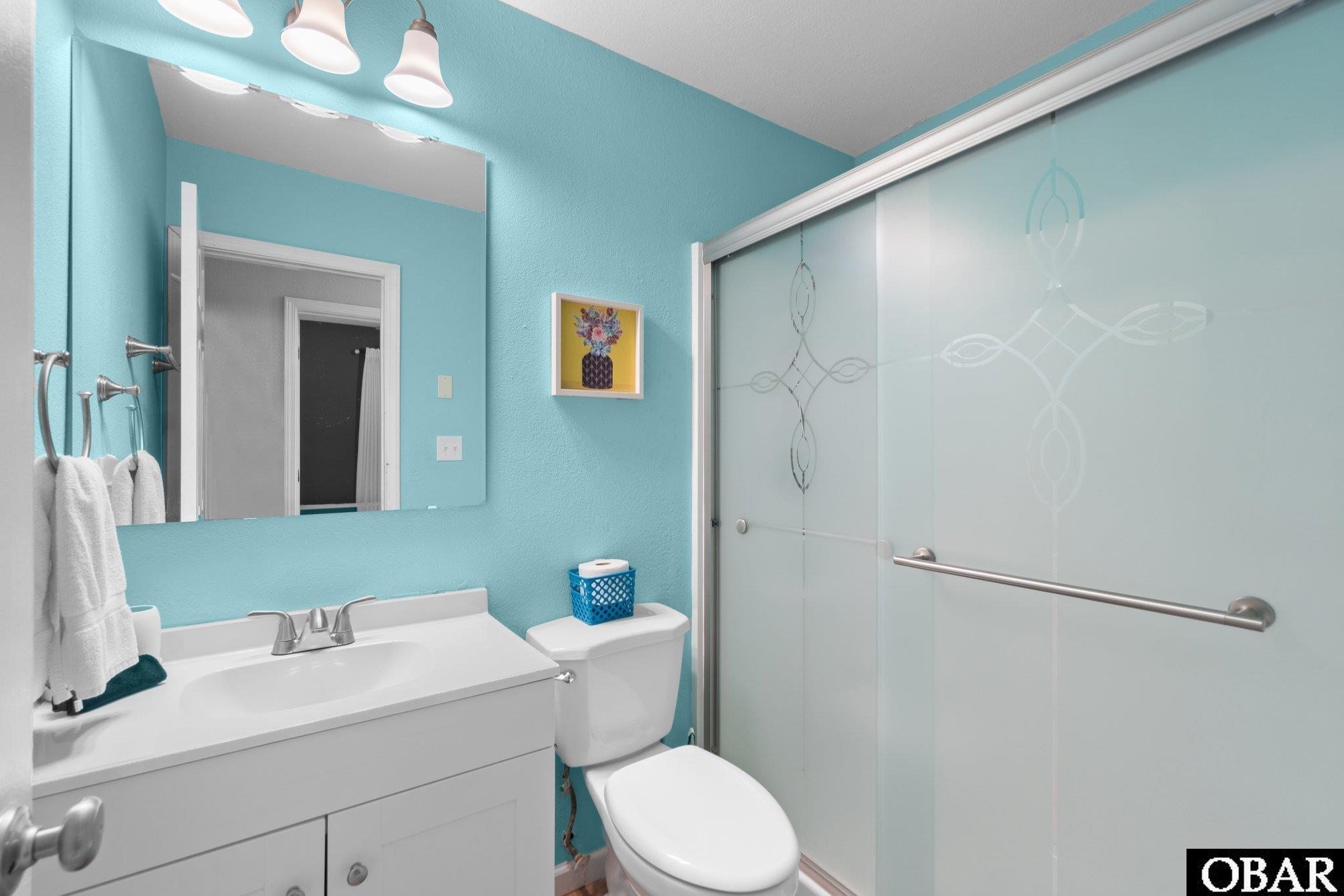 Bathroom with turquoise walls, white vanity, and patterned frosted-glass shower doors.