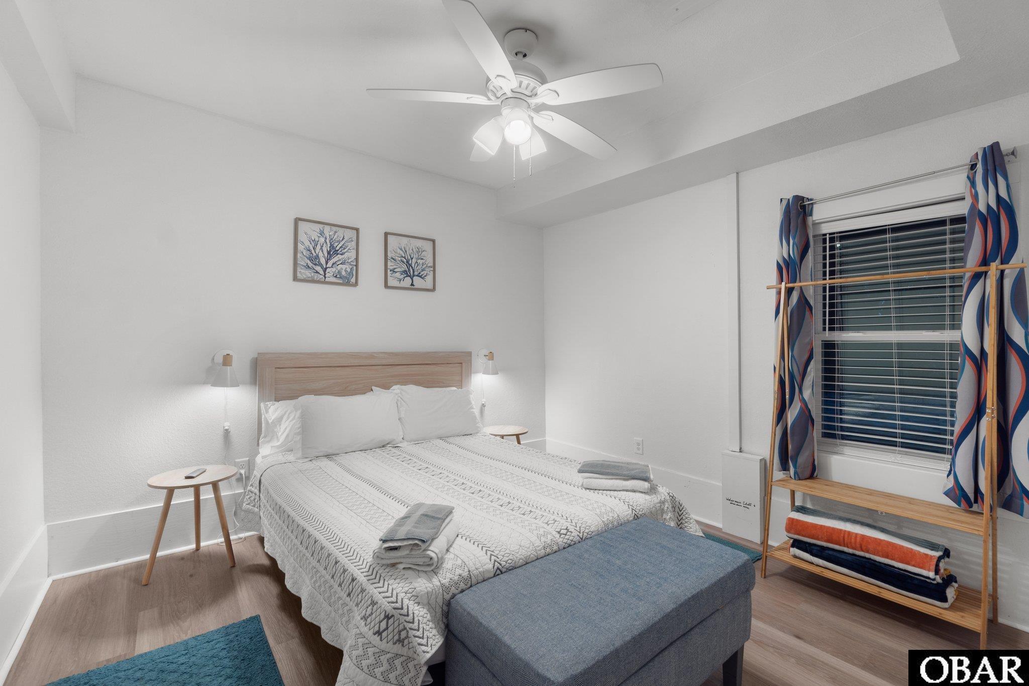 Bedroom with a king-size bed, blue upholstered bench, and window framed by patterned curtains.