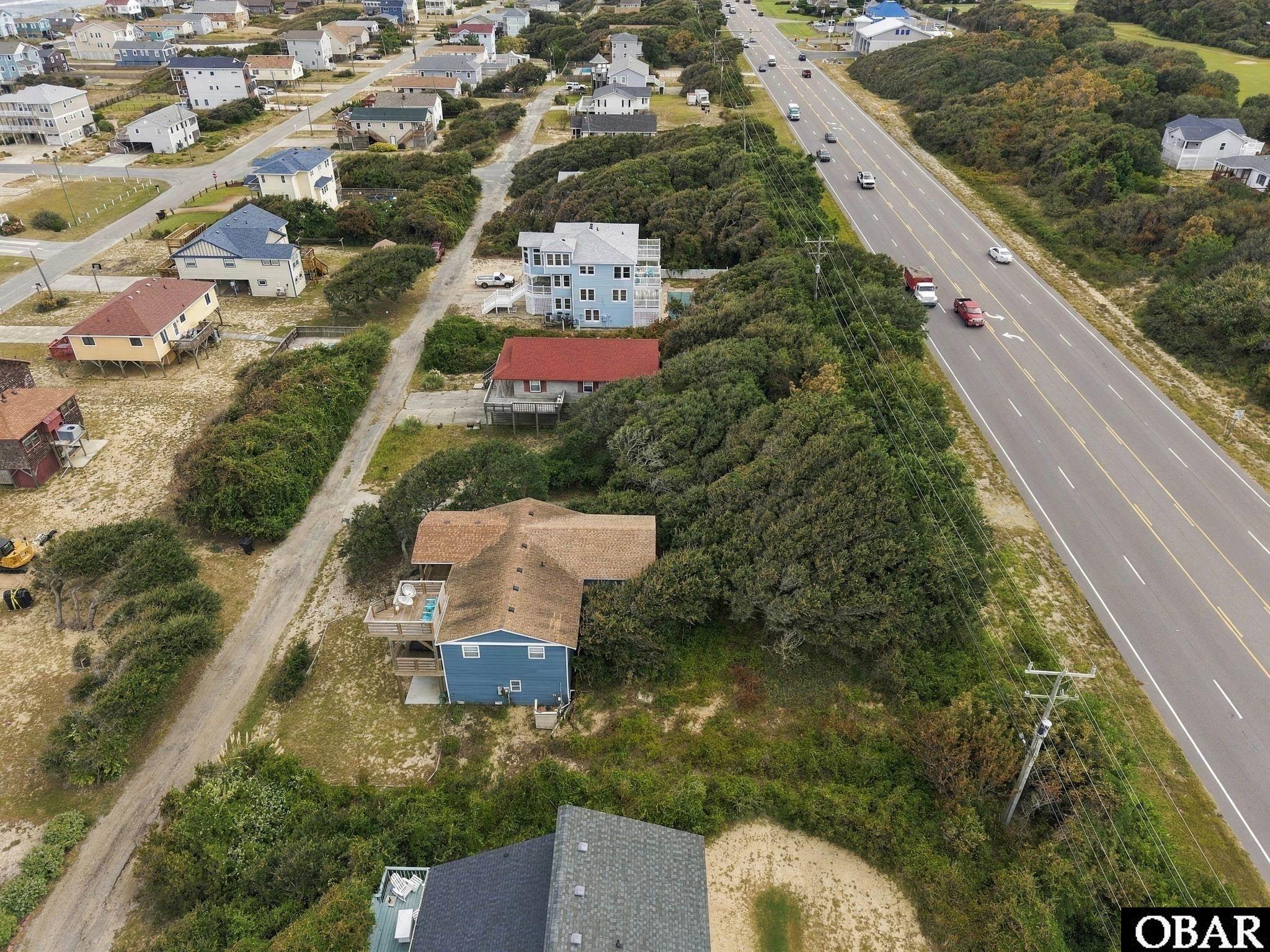 Aerial view of a blue multi-story house among coastal homes beside a highway.
