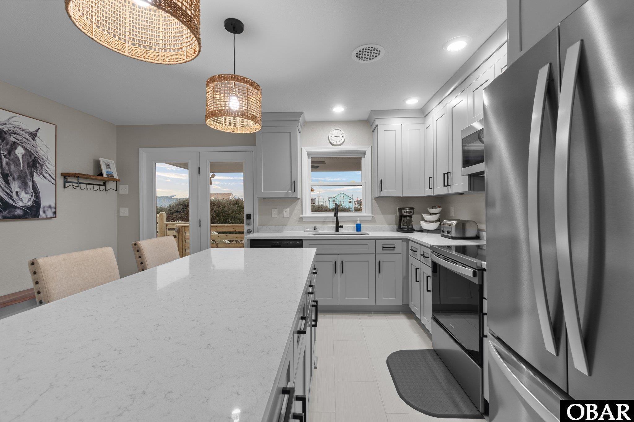 Kitchen with a large white island, gray cabinets, stainless steel appliances, and water visible through the window.