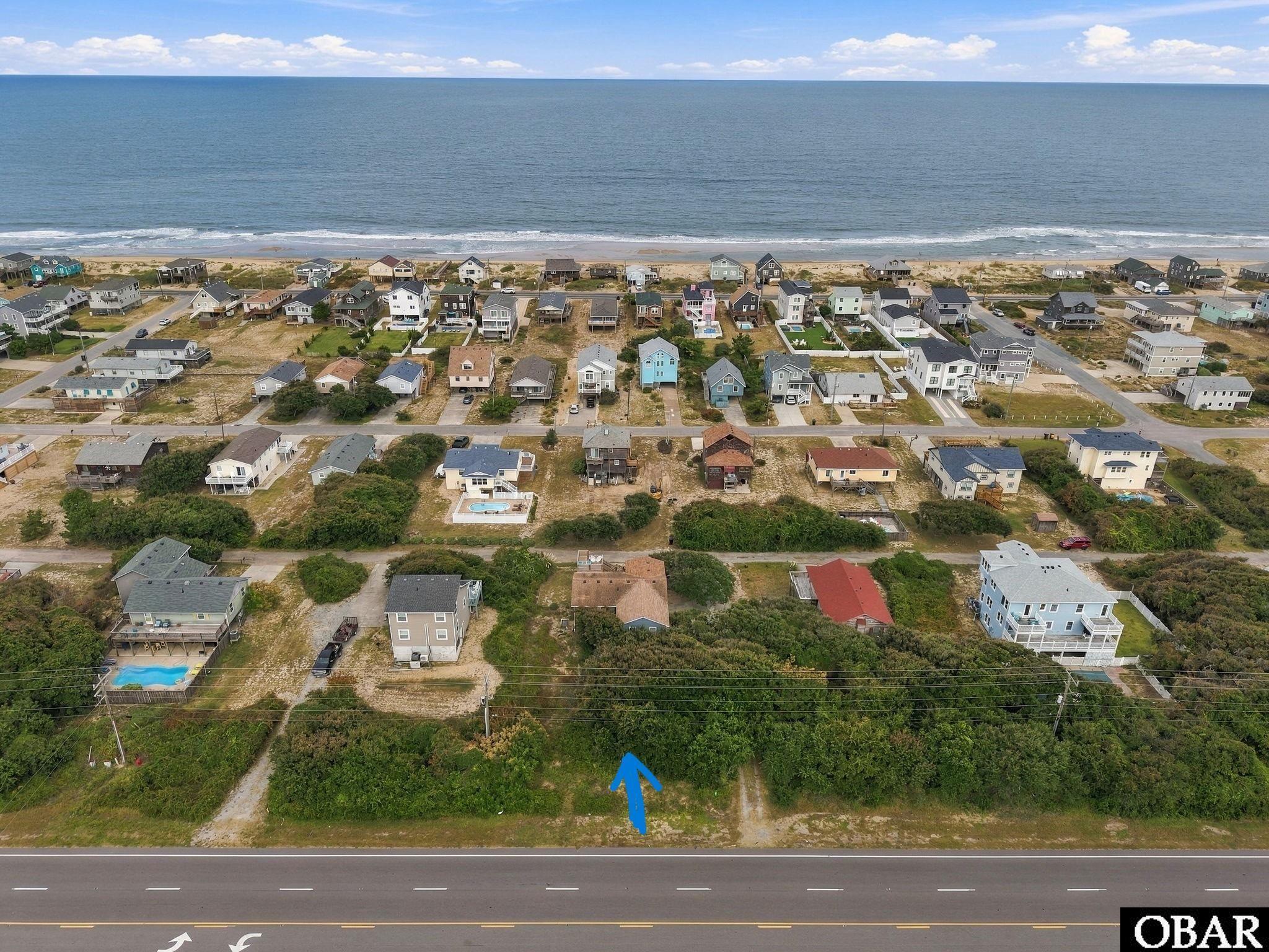 Wooded lot marked with a blue arrow, with coastal homes and ocean in the background.
