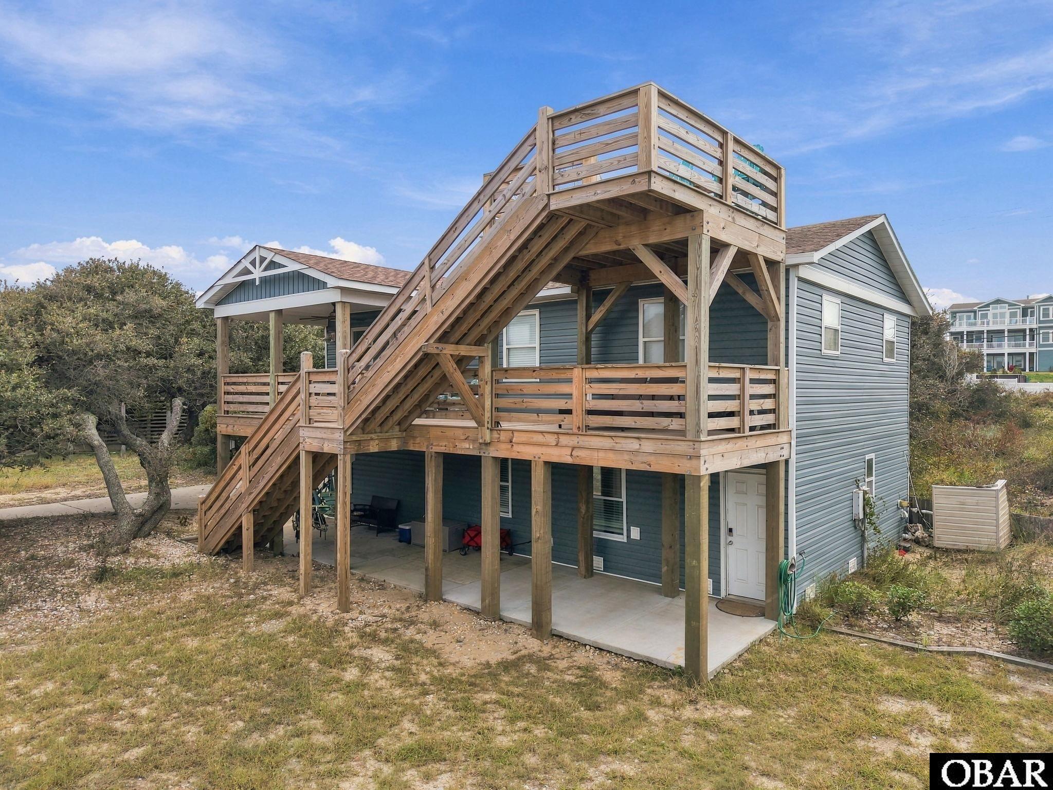 Blue-gray house with a large elevated wooden deck, multiple staircases, and a covered ground-level patio.