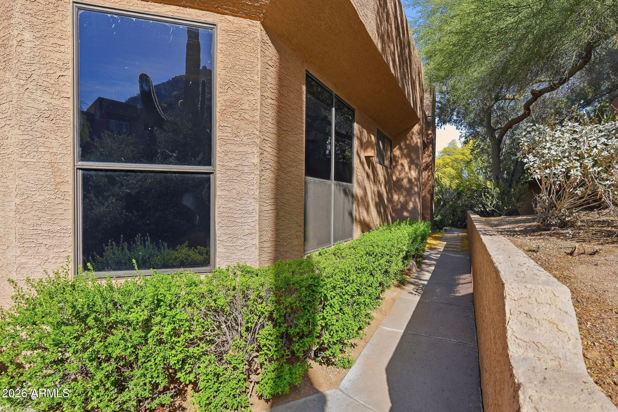 Stucco residence exterior with a walkway bordered by hedges and a low wall.