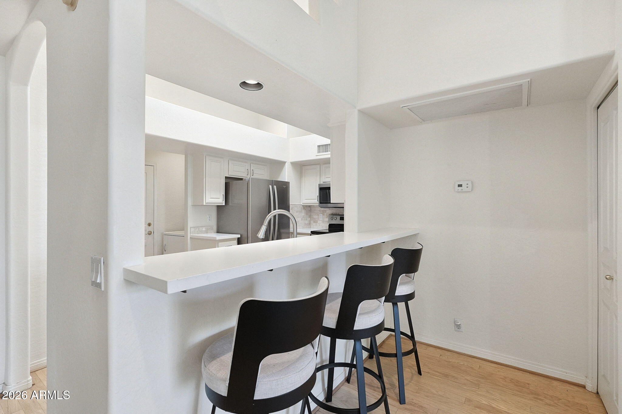 Modern kitchen with a long breakfast bar, three stools, white cabinets, and stainless steel appliances.