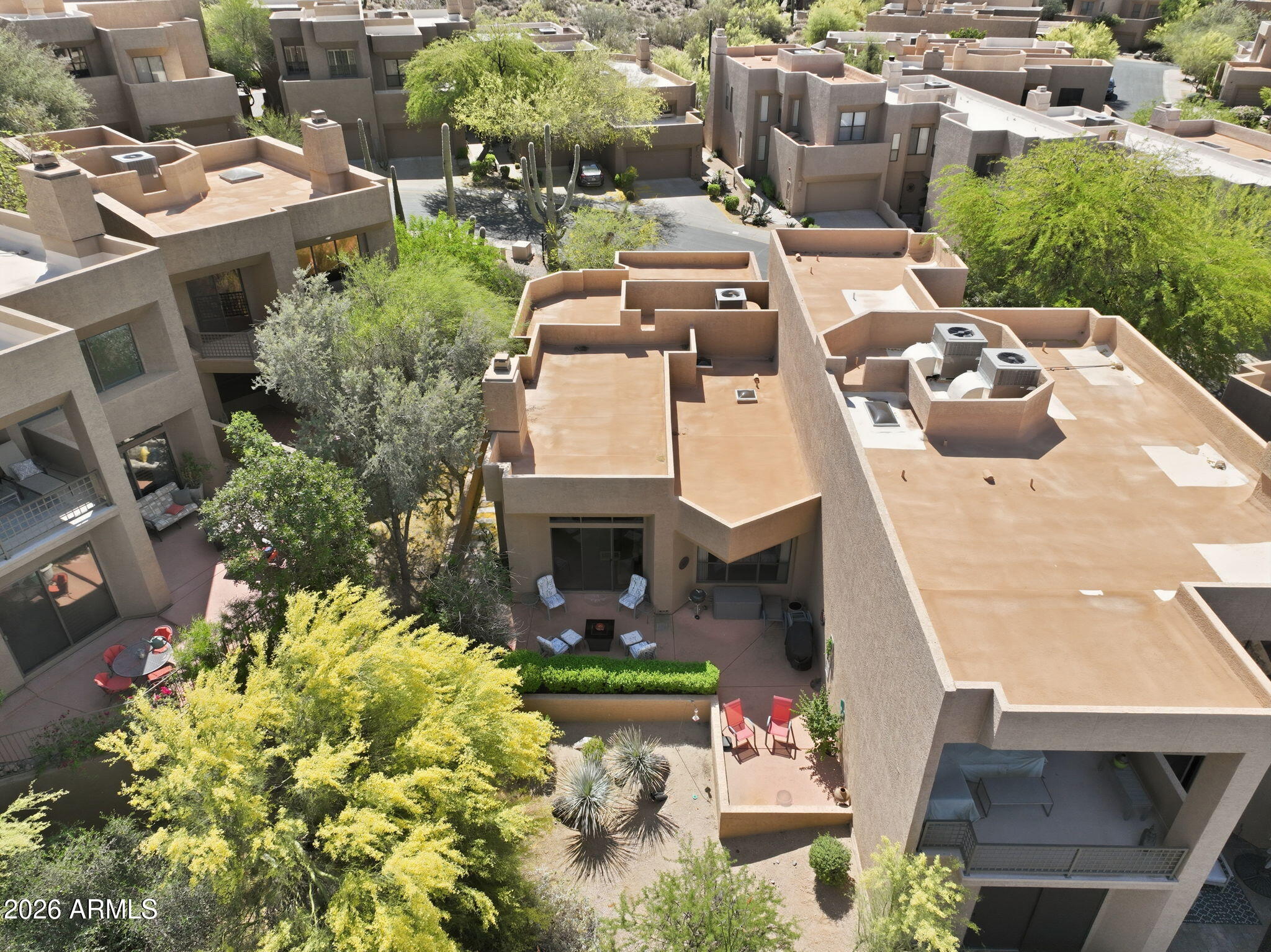 Aerial view of tan homes with flat roofs, private patios, and mature desert landscaping.