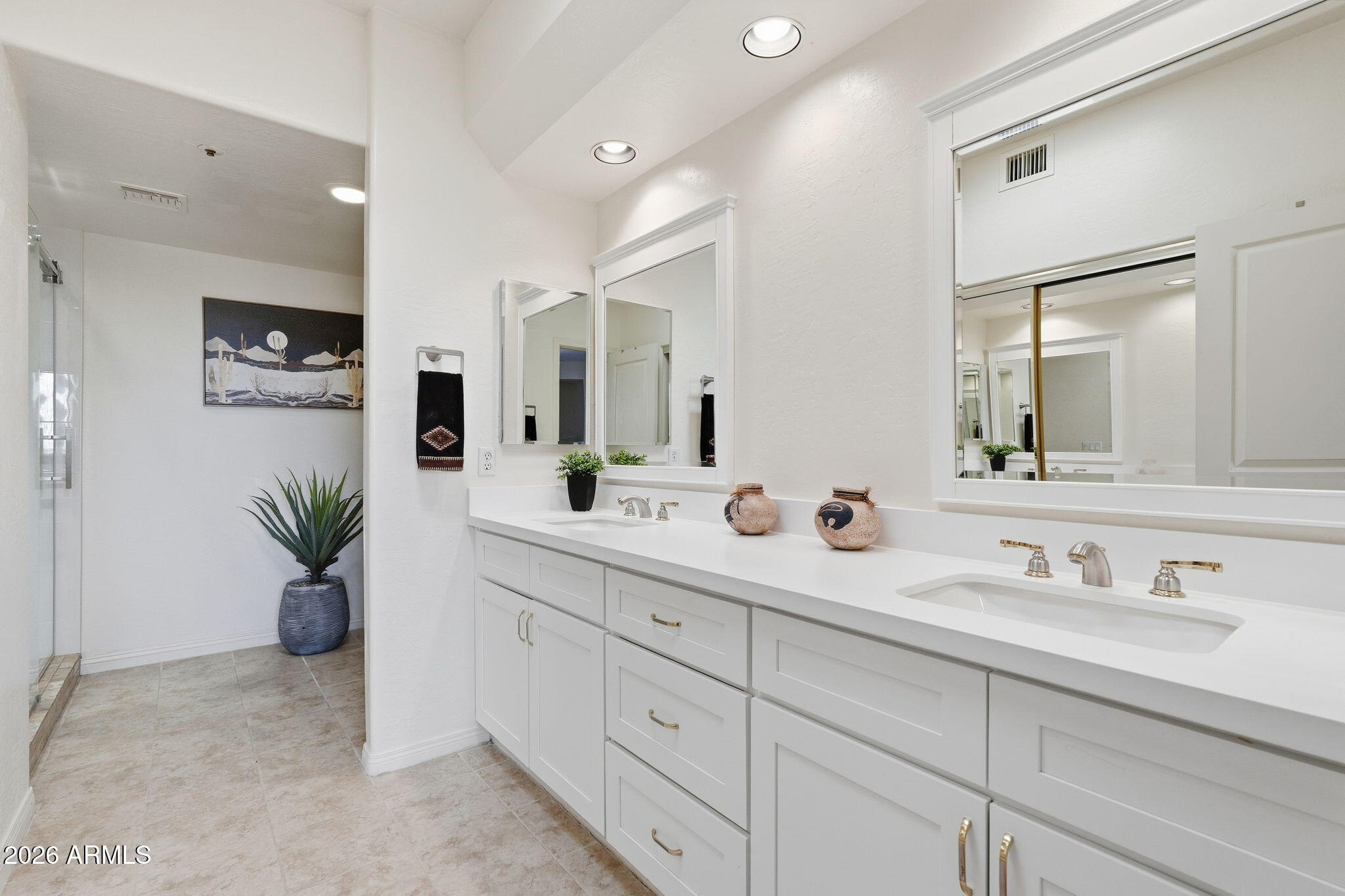 Bright bathroom with a long double-sink vanity, large mirrors, and glass-enclosed shower.