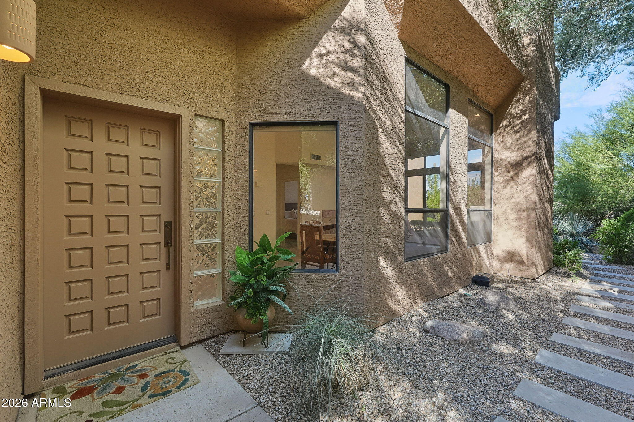 Home entrance with a paneled door, tall windows, desert landscaping, and a stepping-stone path.