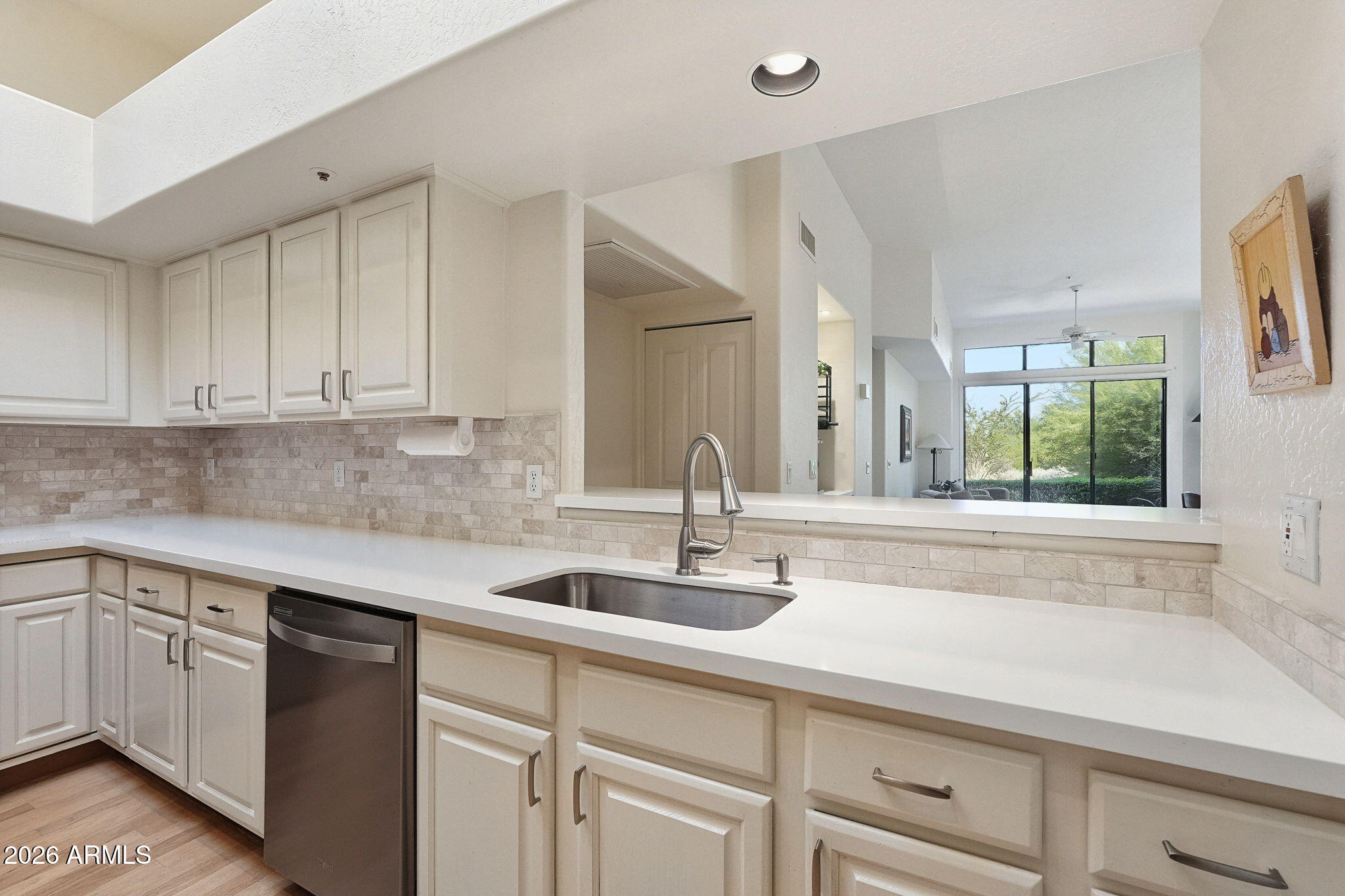 Kitchen with white shaker cabinets, stone-tile backsplash, and a pass-through to a windowed living area.