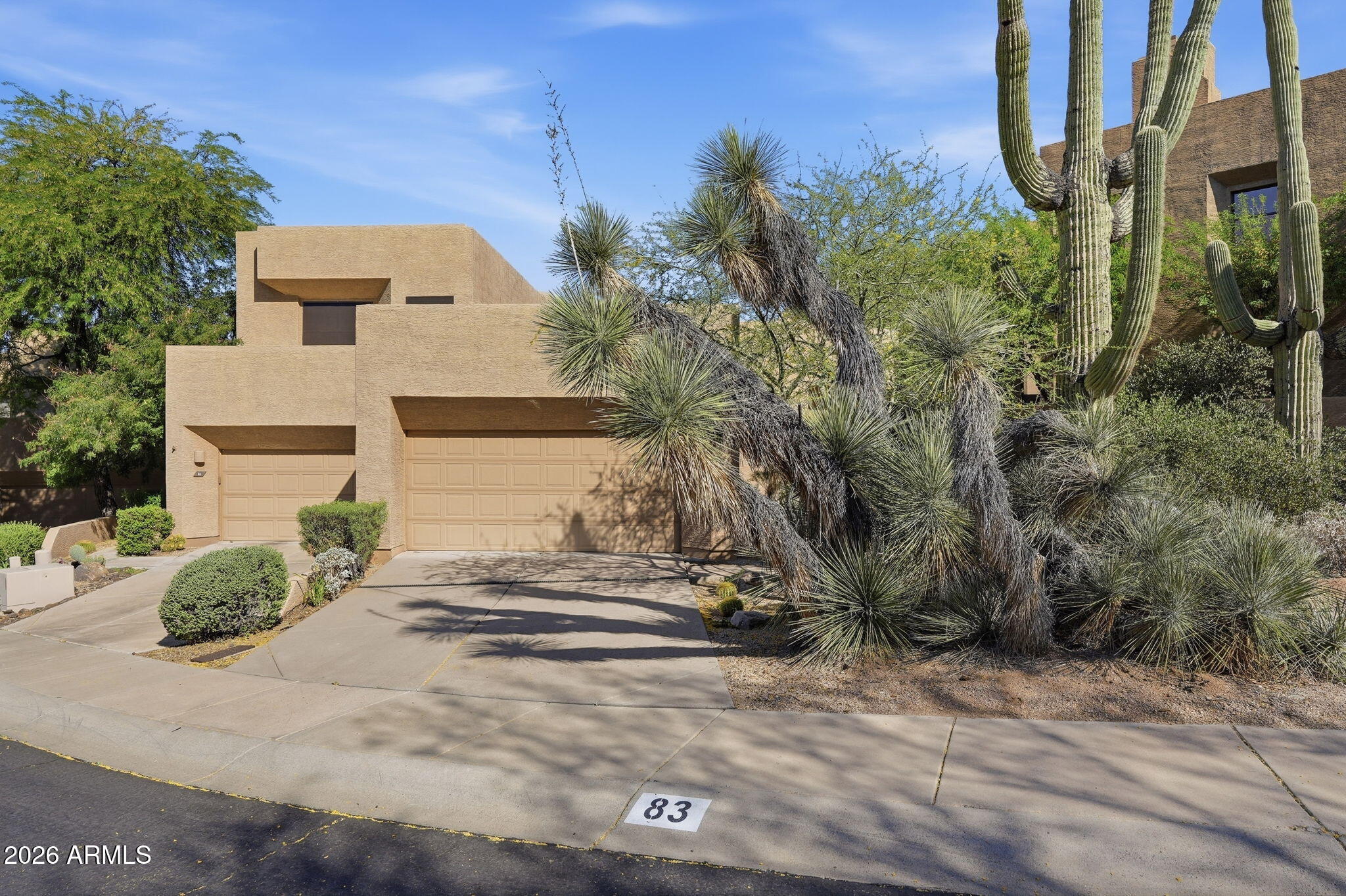 Tan stucco home with a two-car garage, desert landscaping, and sidewalk marker 83.