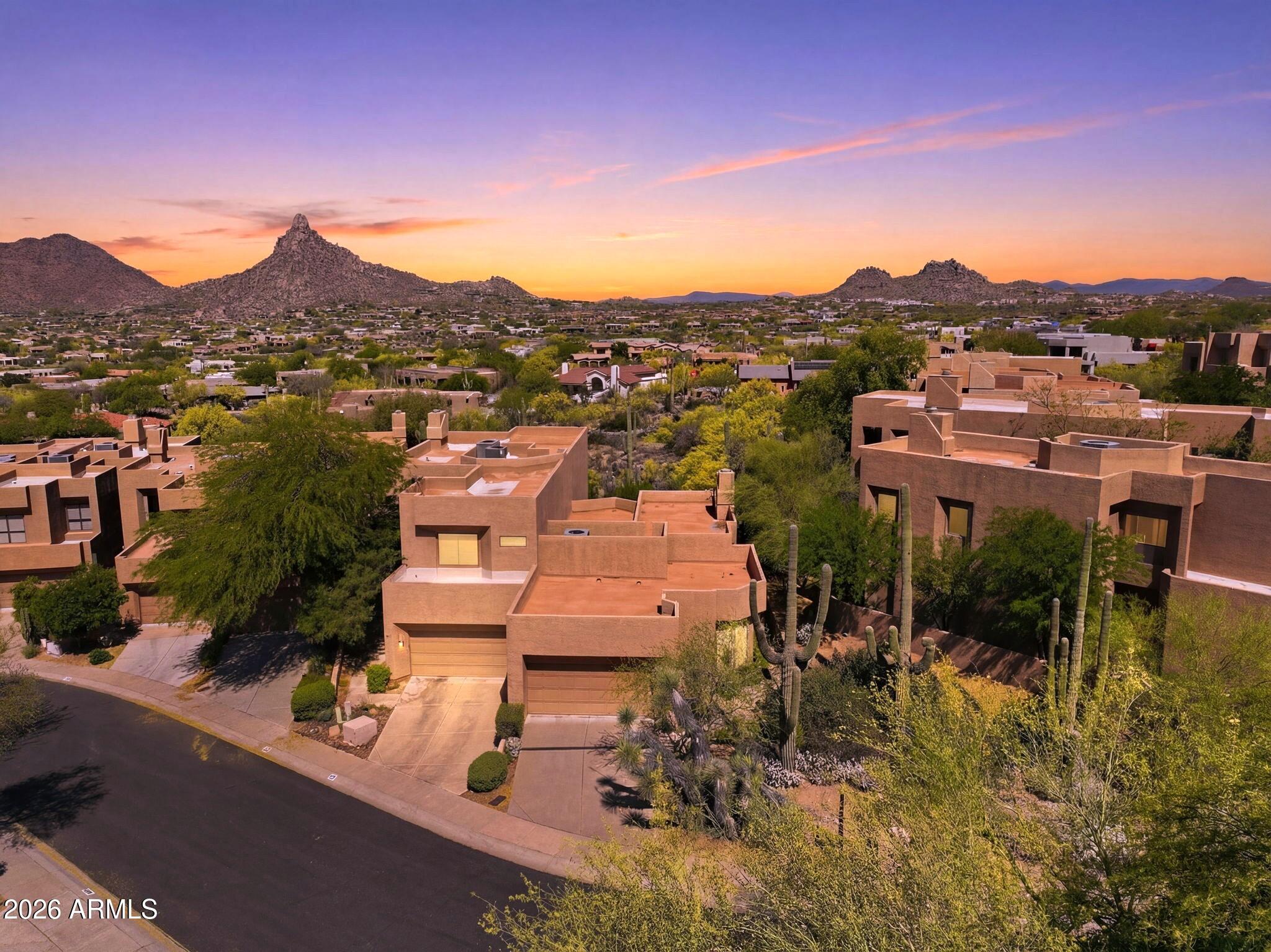 Aerial view of Southwestern homes and desert landscaping, with rocky mountains under a colorful sunset sky.