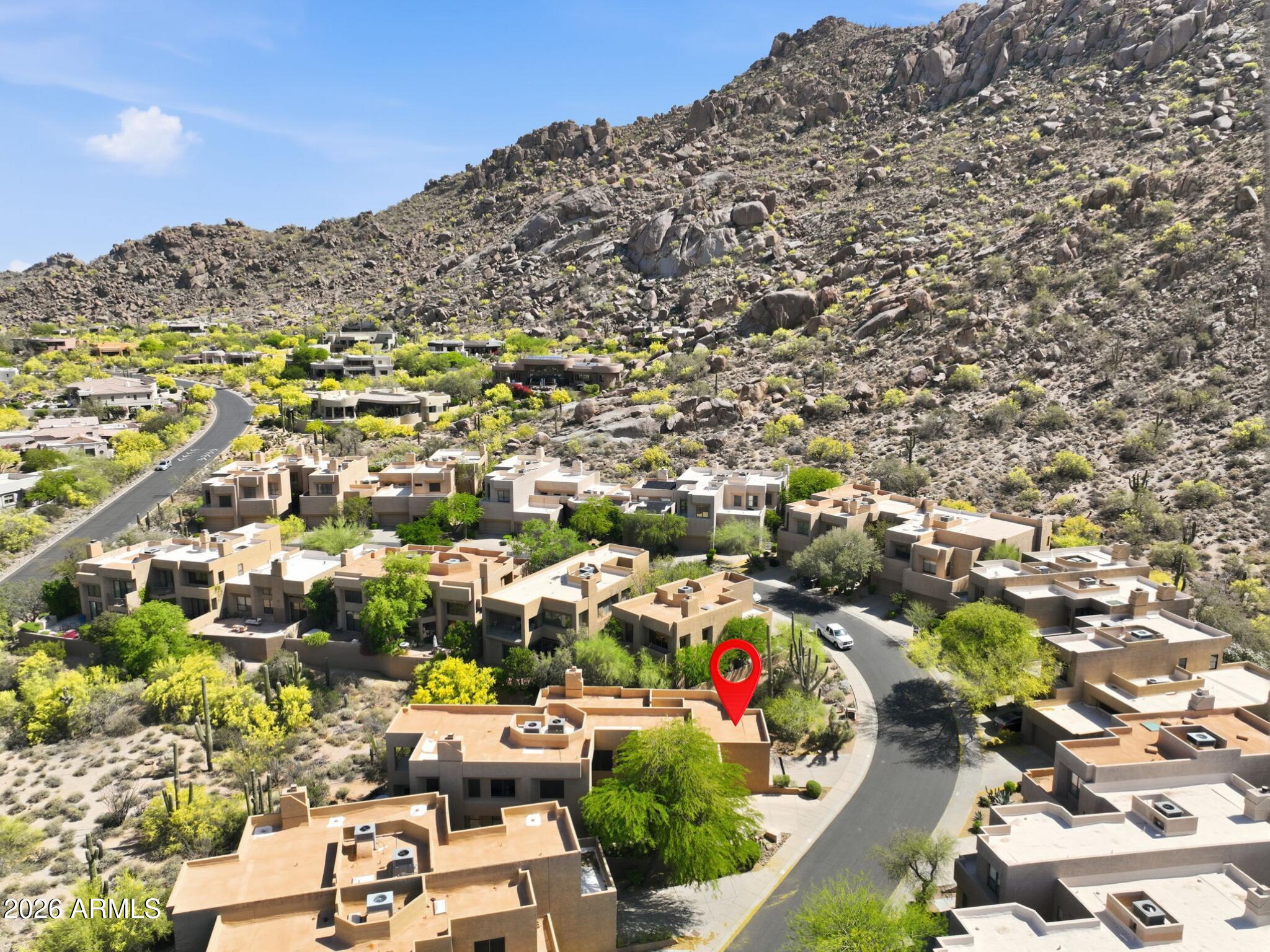 Aerial view of tan homes at the base of rocky desert mountains, with a red pin marking one property.